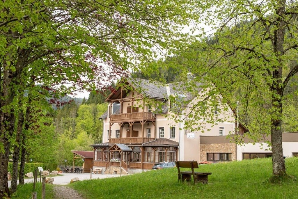 Ein großes Gebäude mit Holzbalkonen, umgeben von grünen Bäumen und einer Wiese mit einer Bank im Vordergrund.