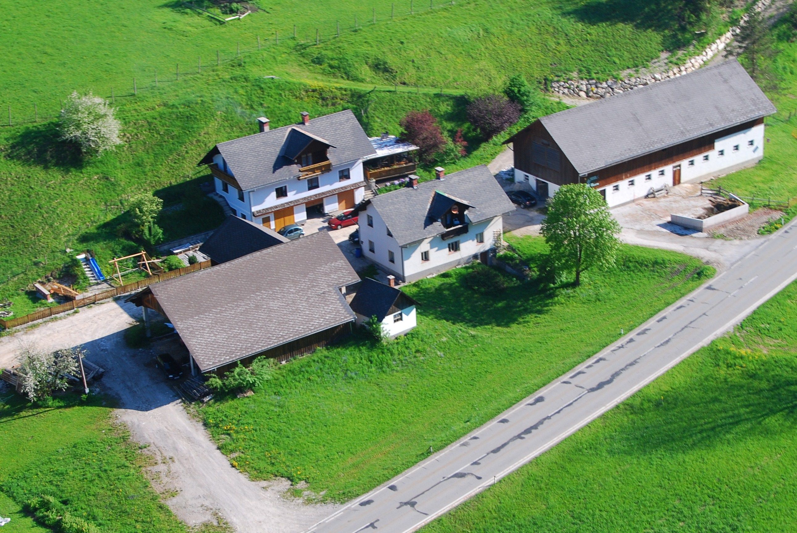 Luftaufnahme eines Bauernhofs mit mehreren Gebäuden und grünen Wiesen.