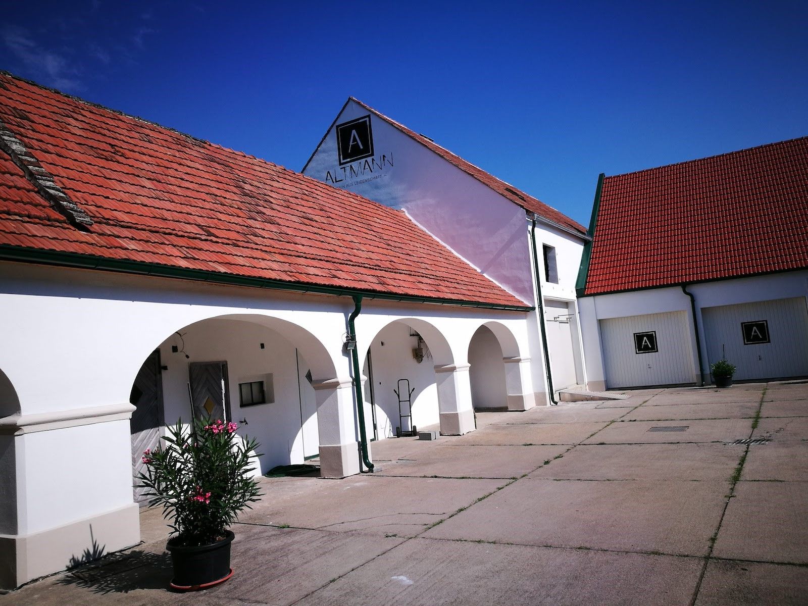 Weißes Gebäude mit roten Ziegeldächern und Arkaden, blauer Himmel.