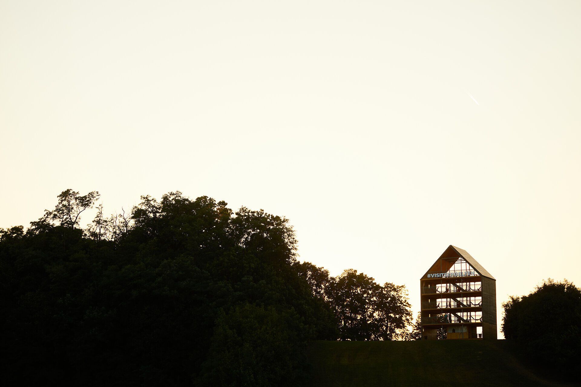 Ein beeindruckendes Flederhaus thront majestätisch auf dem Eisberg, umgeben von üppigem Grün und sanften Hügeln. Die goldene Abendsonne taucht die Landschaft in warmes Licht und schafft eine friedliche Atmosphäre, die zum Verweilen einlädt. Hier, wo Natur und Architektur harmonisch verschmelzen, eröffnet sich ein Paradies der Blicke.