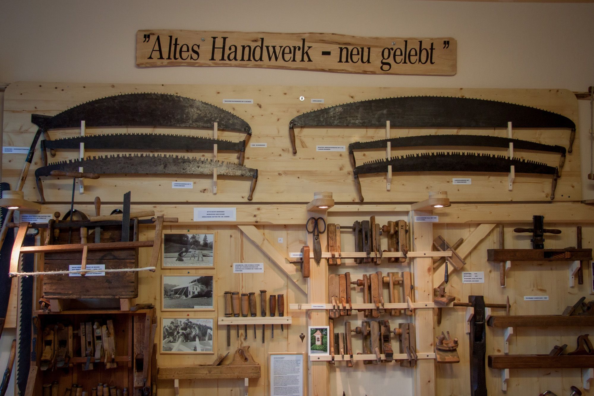 Ausstellung von alten Handwerkzeugen an einer Holzwand mit dem Schild 'Altes Handwerk - neu gelebt'.