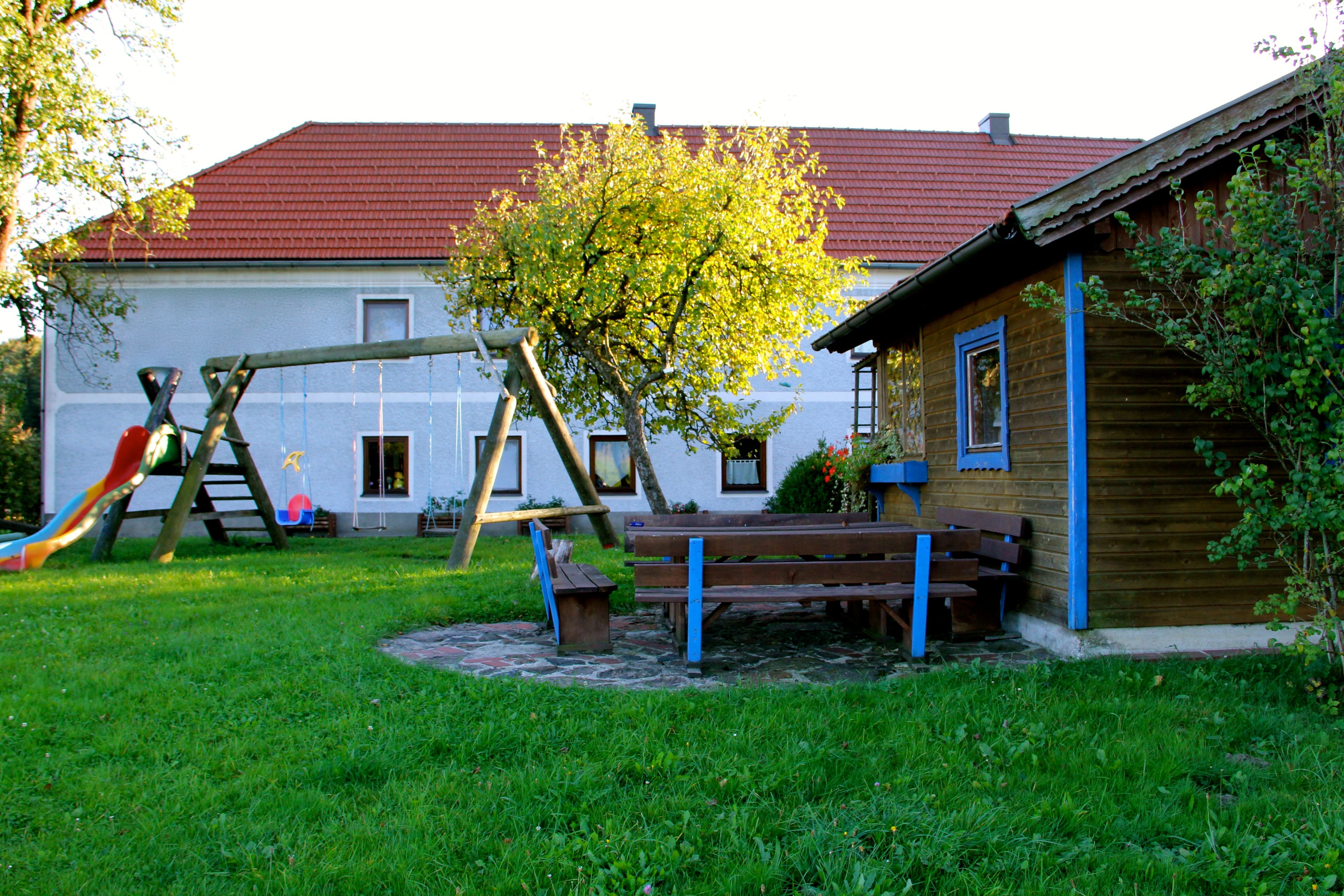 Ein Spielplatz mit Schaukel, Rutsche und Sitzbänken vor einem Haus mit rotem Dach.