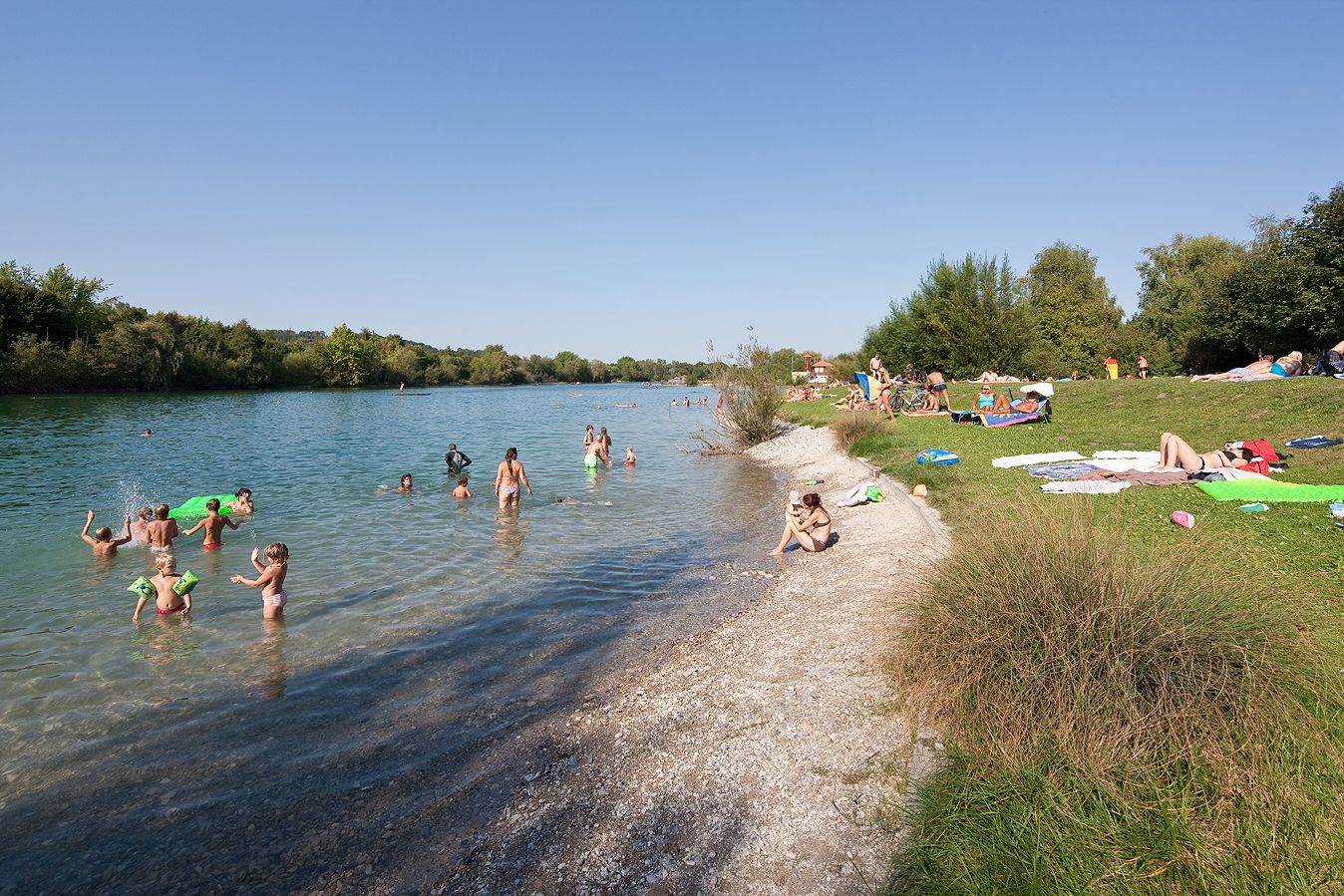 Menschen schwimmen und entspannen am Ratzersdorfer See an einem sonnigen Tag.