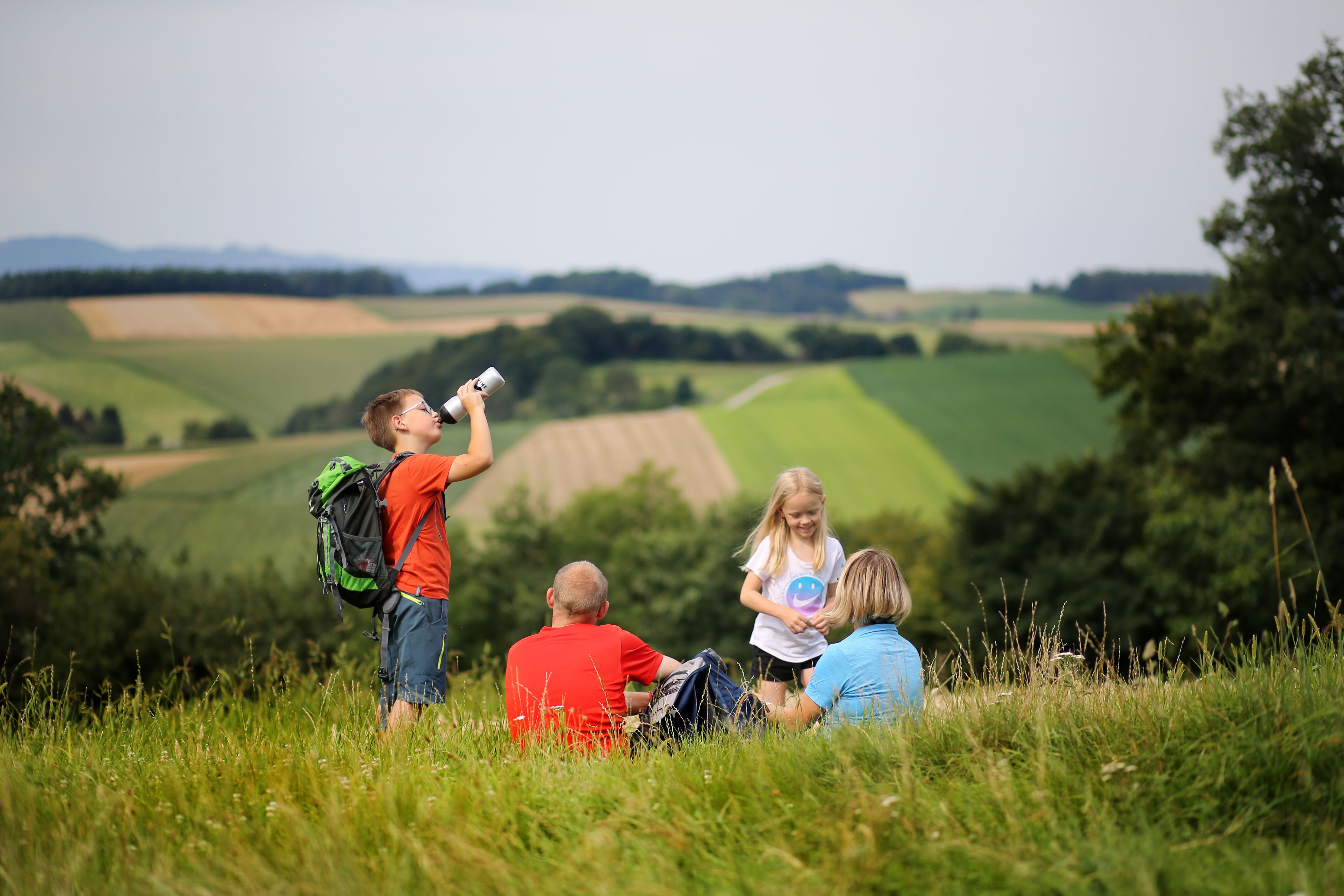 Familie macht Wanderpause entlang der Dunkelsteinerwald-Runde. Im Hintergrund erstreckt sich die Landschaft.