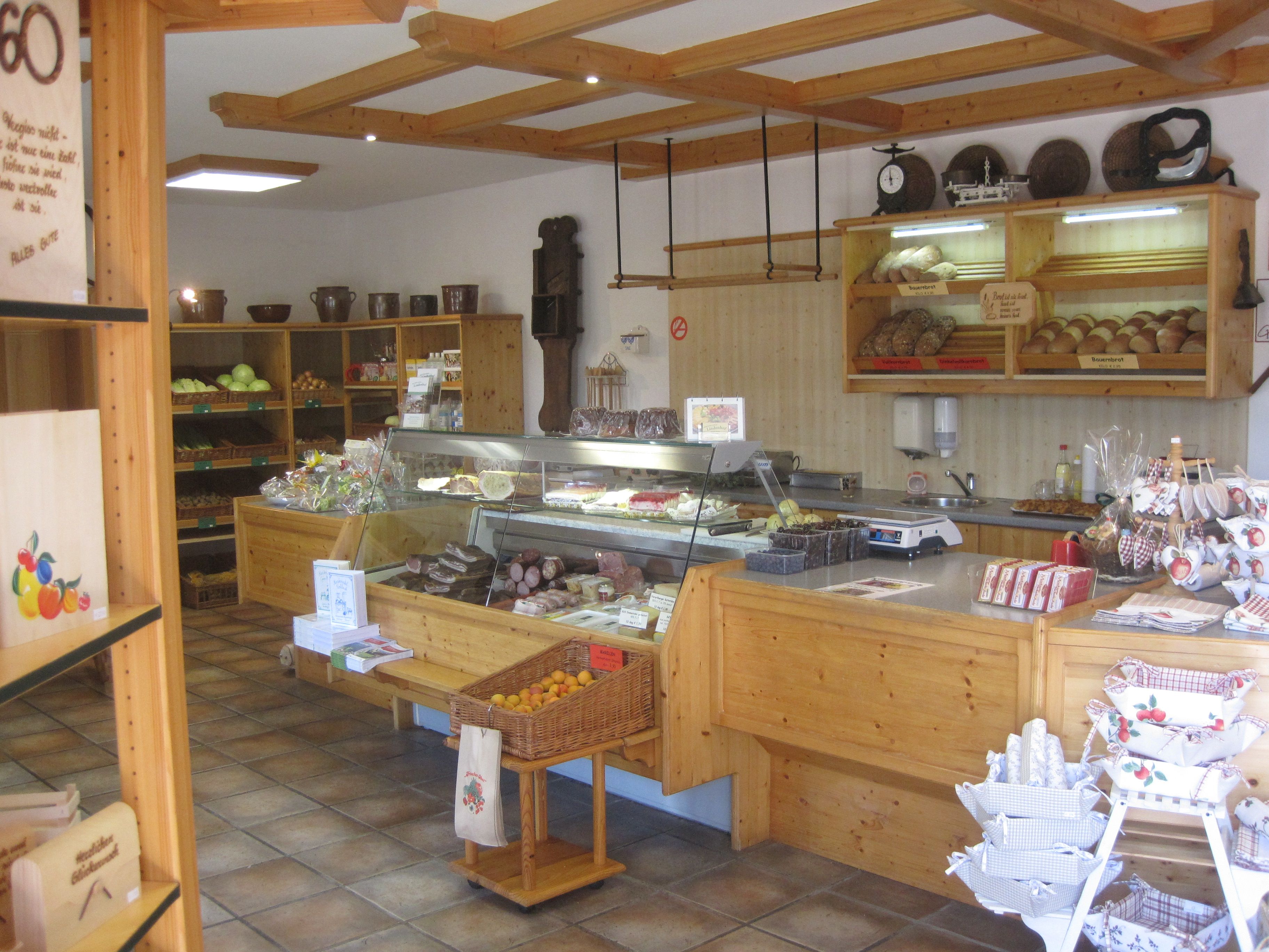 Innenansicht eines Bauernladens mit Holzregalen, gefüllt mit Brot, Obst und Wurstwaren.