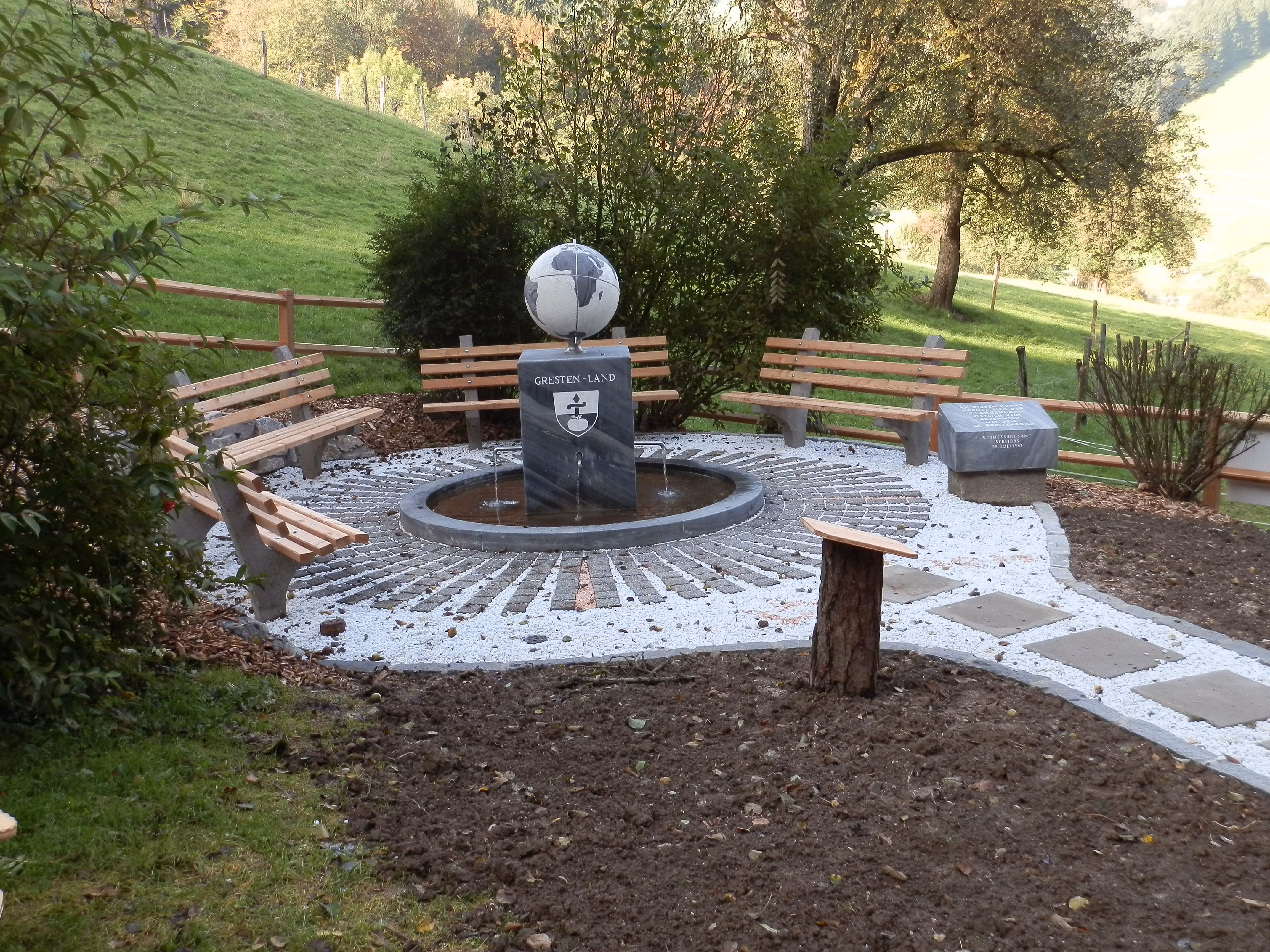 Ein Rastplatz mit Bänken und einem Meridianstein in einer ländlichen Umgebung.