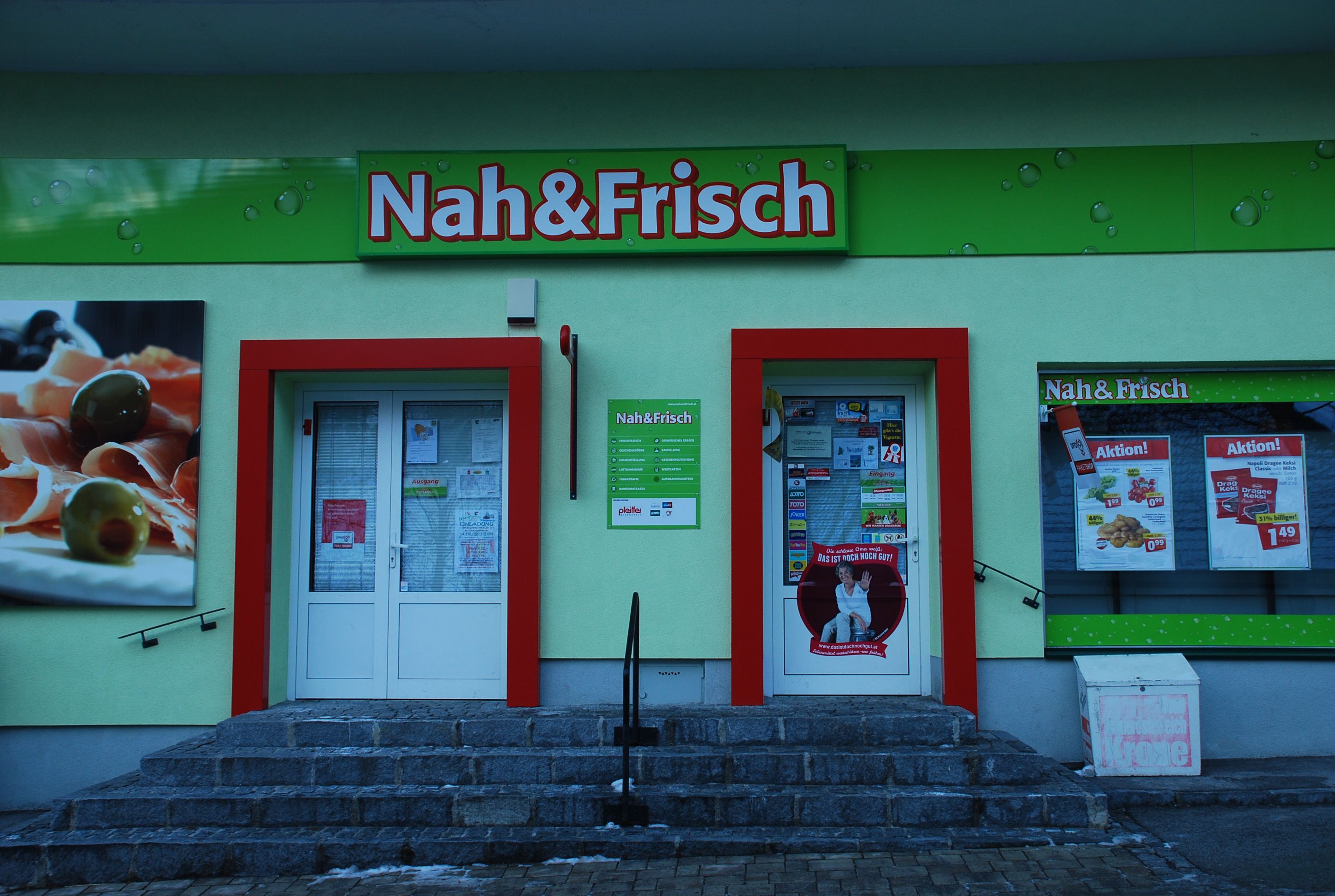 Eingang eines Nah&Frisch-Ladens mit Werbeplakaten und Schaufenster.
