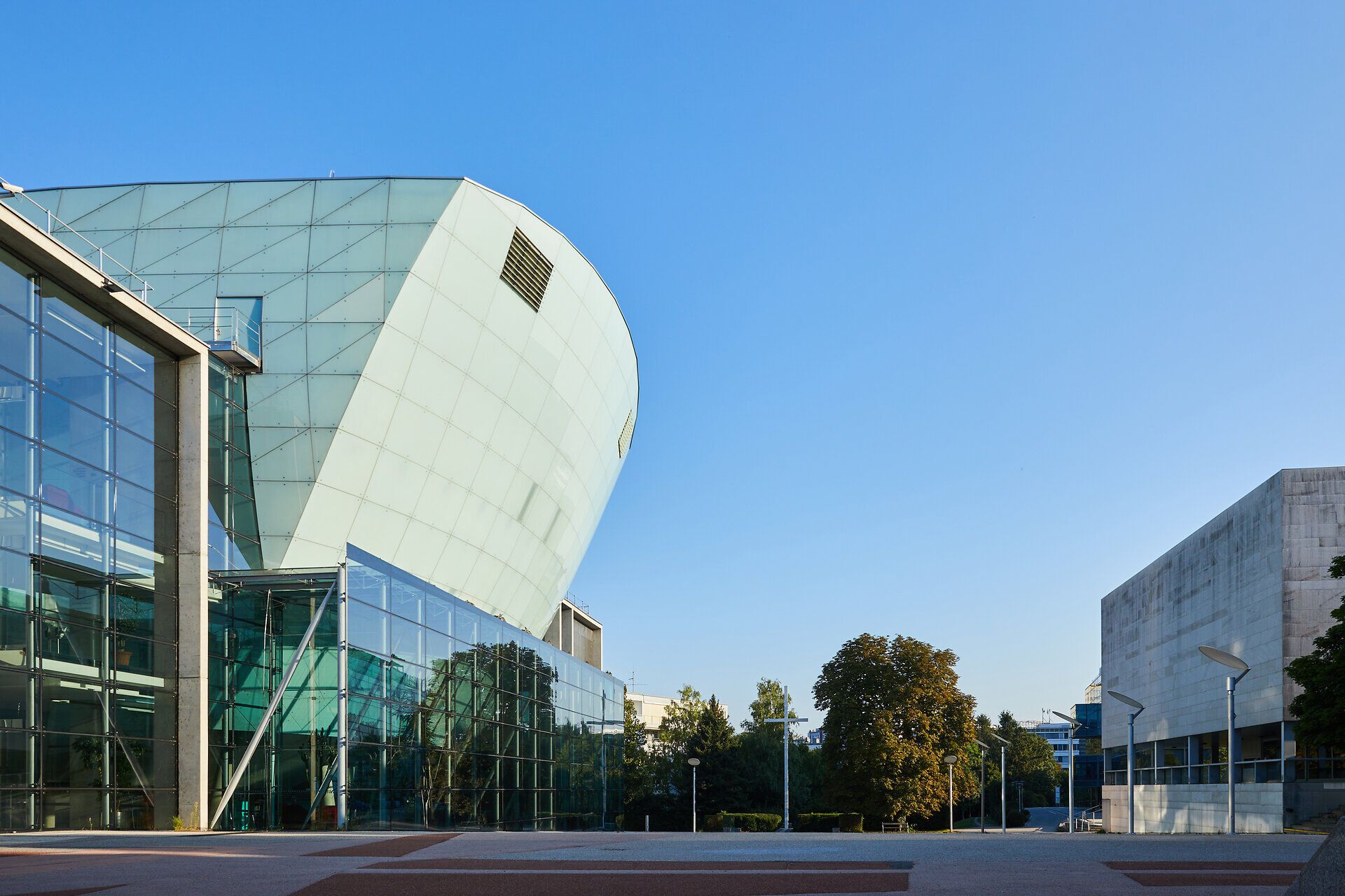 Die moderne Architektur strahlt eine harmonische Verbindung von Glas und Beton aus, während die klare, blaue Himmel die Szenerie erhellt. Umgeben von üppigem Grün lädt dieser Ort zum Verweilen und Entspannen ein, perfekt für einen Ausblick auf die Schönheit der Umgebung.