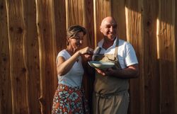 In einer warmen, einladenden Atmosphäre genießen zwei Personen gemeinsam eine kulinarische Kreation. Die Freude am Kochen und die Leidenschaft für regionale Zutaten spiegeln sich in ihren lächelnden Gesichtern wider, während die rustikale Holzverkleidung im Hintergrund eine gemütliche Stimmung schafft.