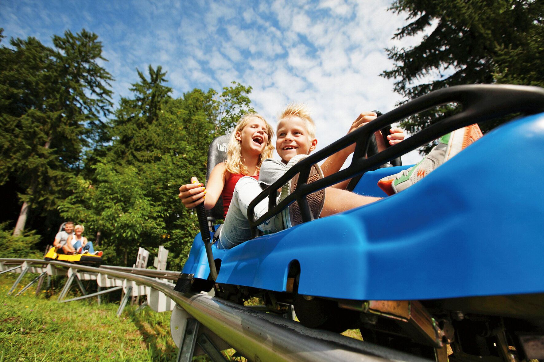 Ein aufregendes Abenteuer erwartet die jungen Entdecker auf der Sommerrodelbahn. Lachen und Freude strahlen von ihren Gesichtern, während sie durch die malerische Landschaft sausen. Umgeben von üppigem Grün und strahlend blauem Himmel, ist dies der perfekte Ort für unvergessliche Erlebnisse.