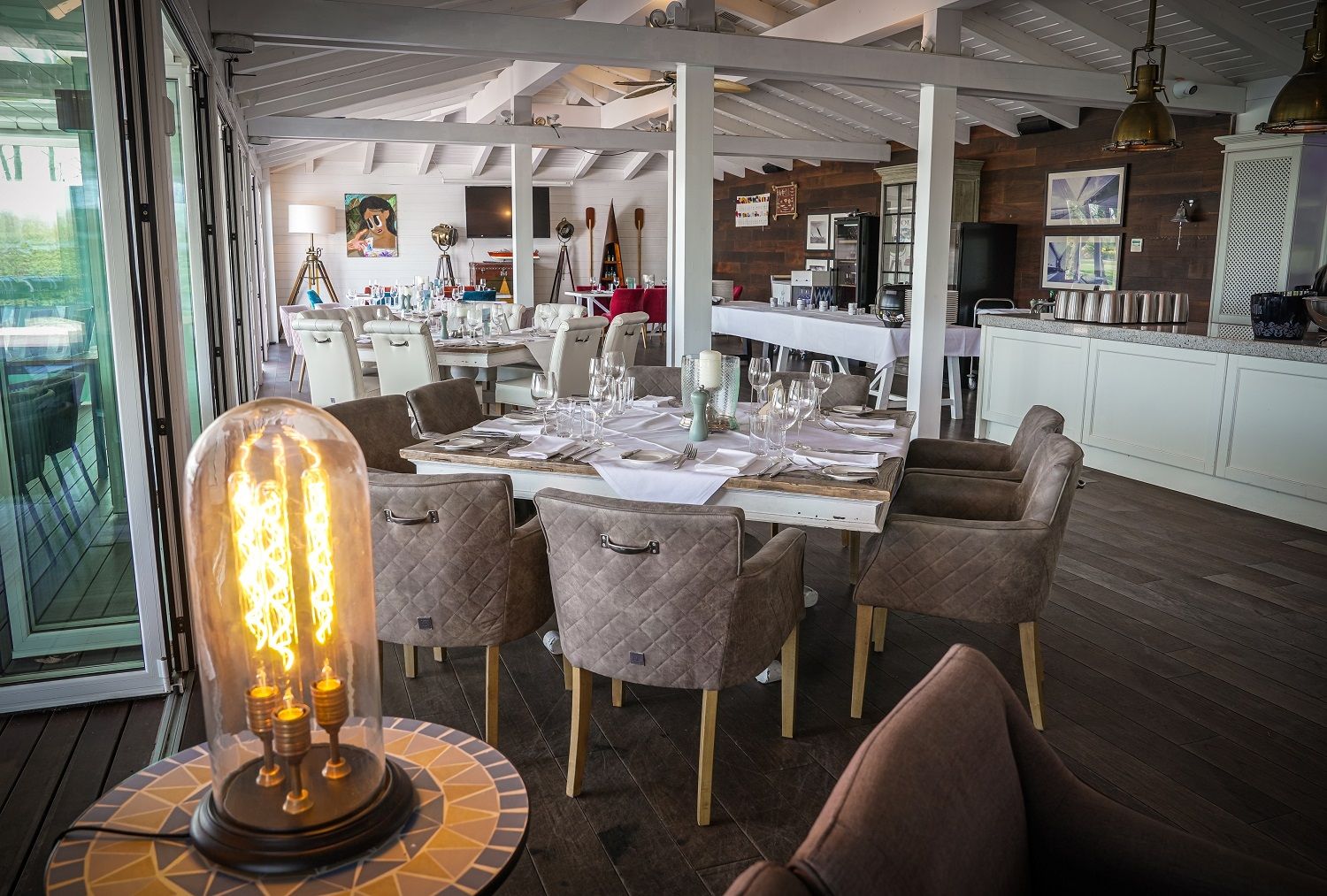 Gedeckter Tisch im Speisesaal. IM Vordergrund eine Leuchte. Der Saal ist in Weiß und braun gehalten.