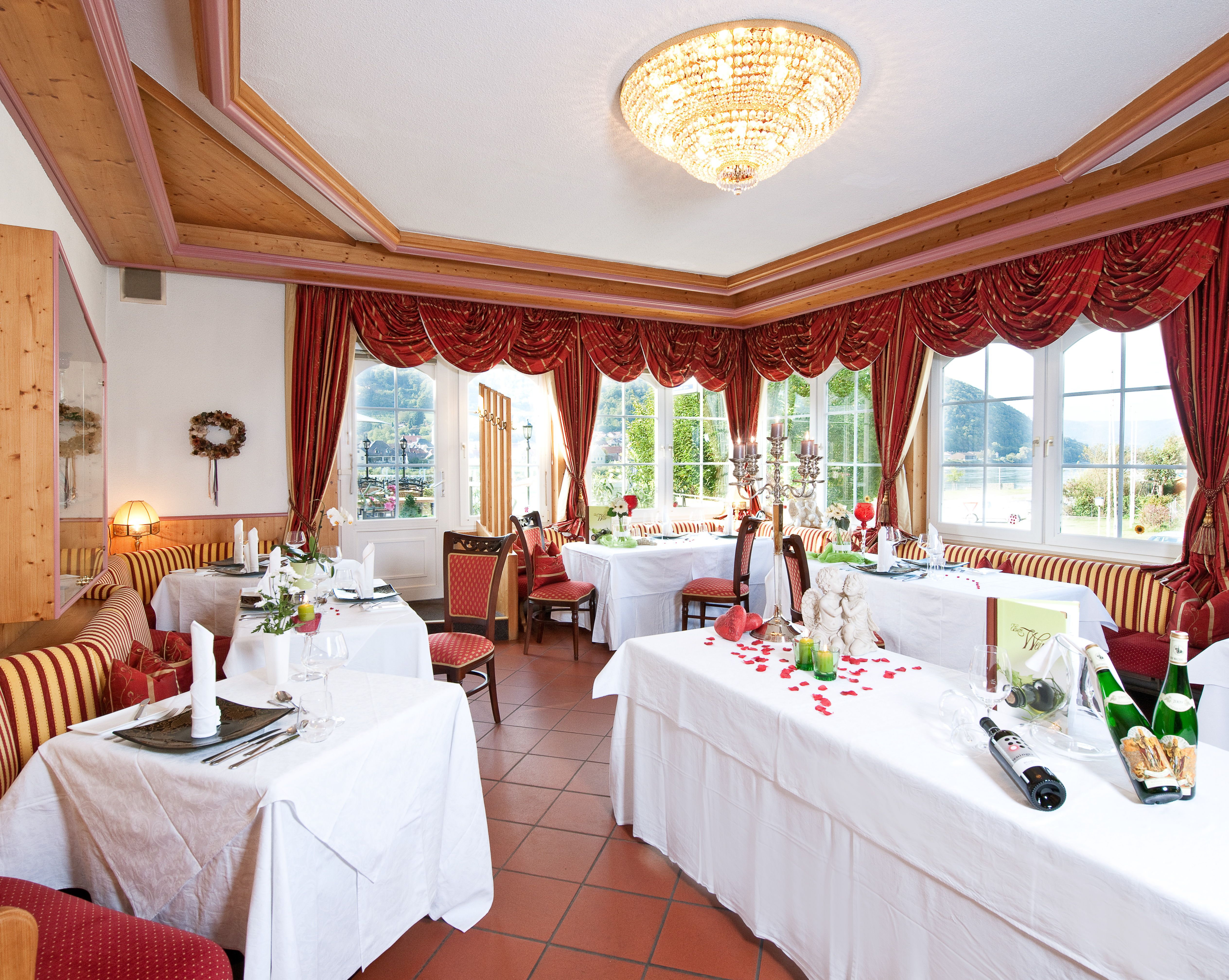 Elegantes Restaurant mit gedeckten Tischen, roten Vorhängen und Kronleuchter.