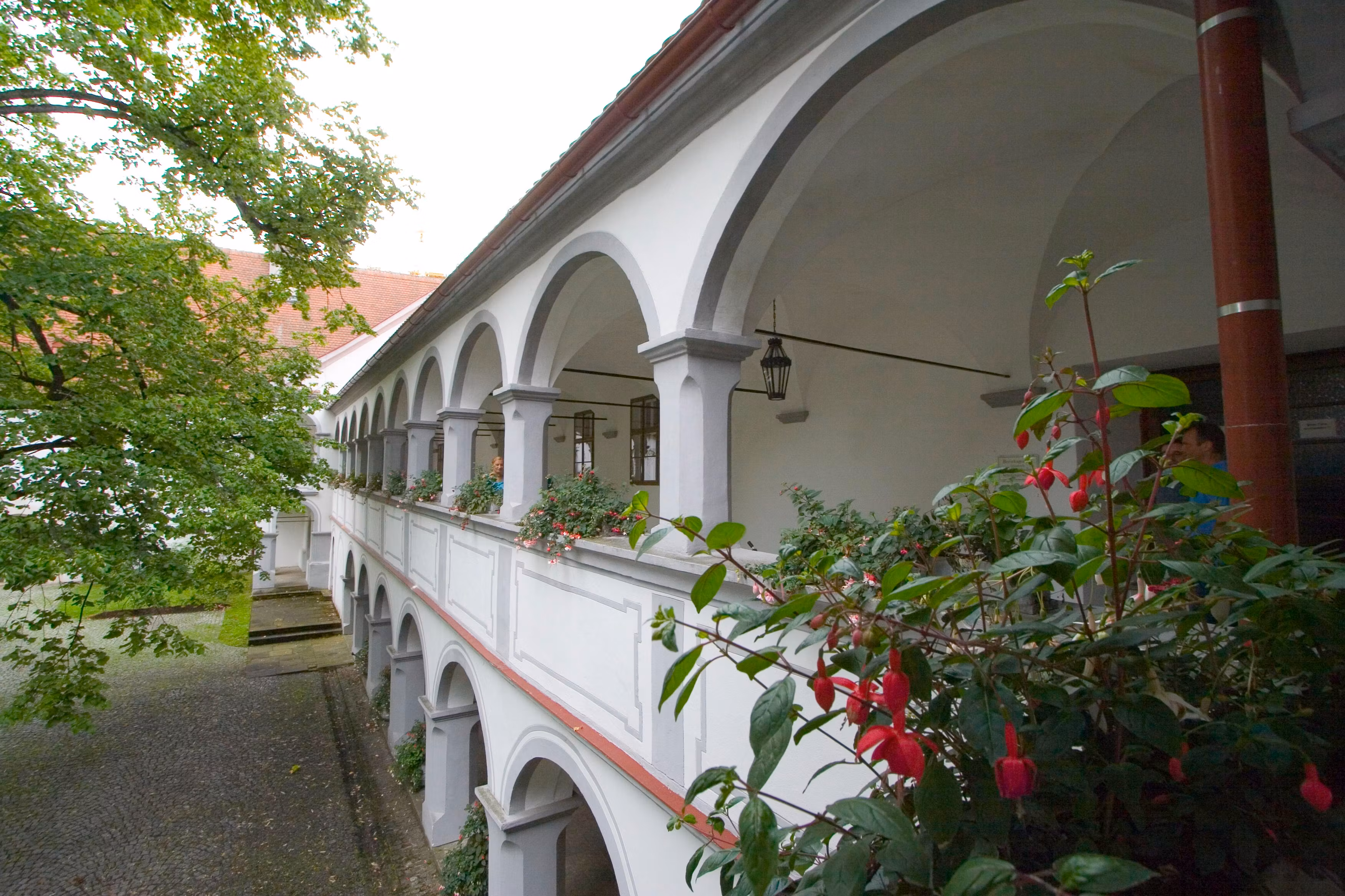 Ein zweistöckiger Arkadengang mit weißen Bögen und Blumen im Schloss Scheibbs.
