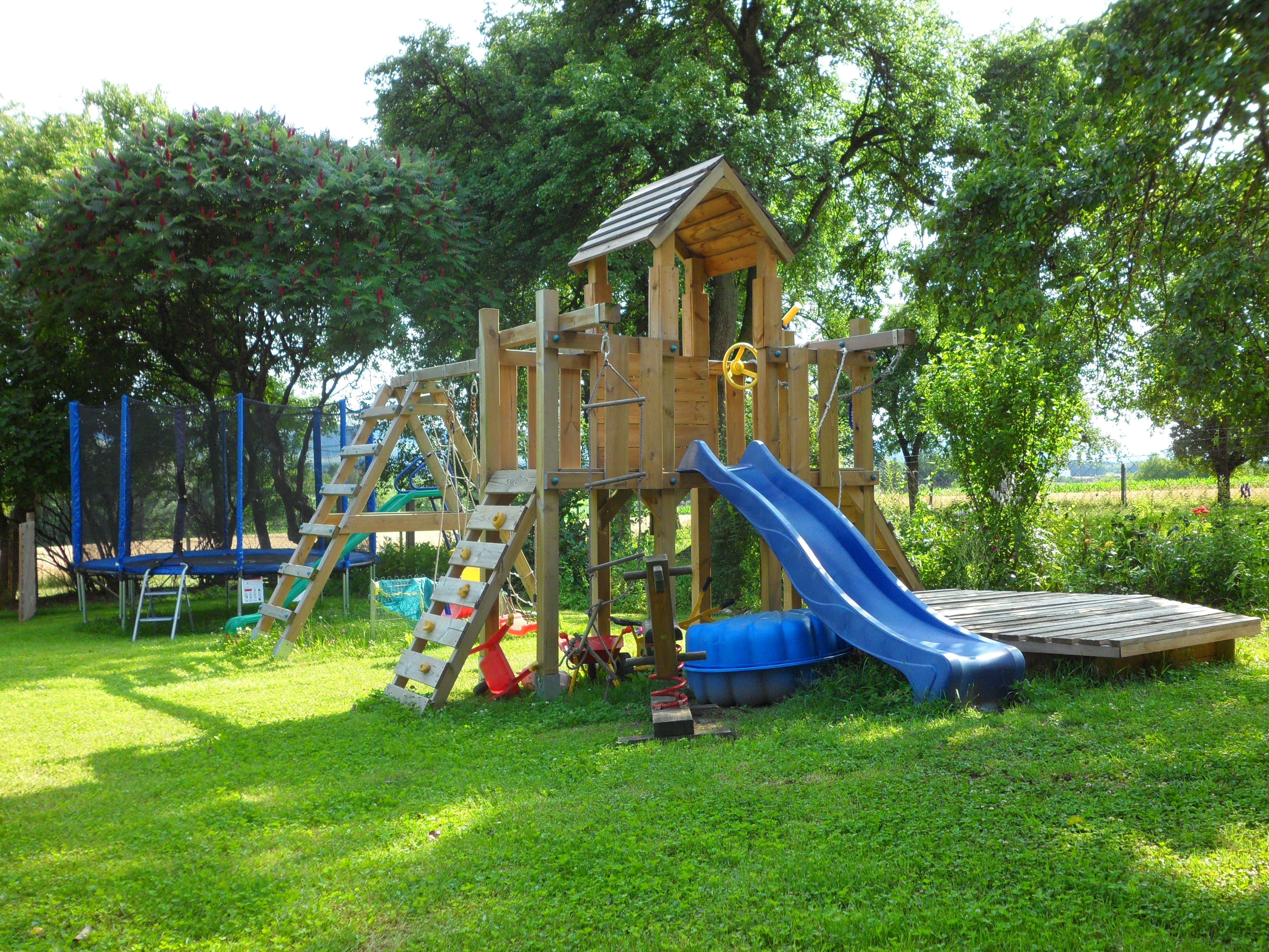 Ein Spielplatz im Garten mit Klettergerüst, Rutsche und Trampolin.