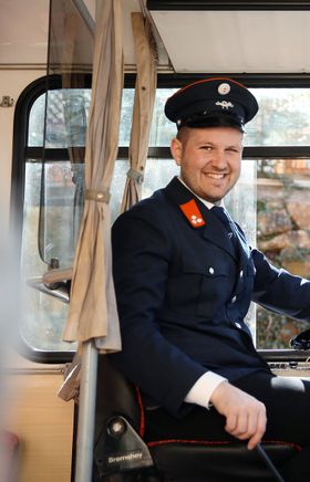 Ein fröhlicher Busfahrer lenkt den Retrobus durch die blühenden Birnbäume der Moststraße. Die sanften Farben der Blüten und die frische Frühlingsluft laden dazu ein, die Schönheit der Region zu erkunden. Genießen Sie die Fahrt und lassen Sie sich von der idyllischen Landschaft verzaubern.