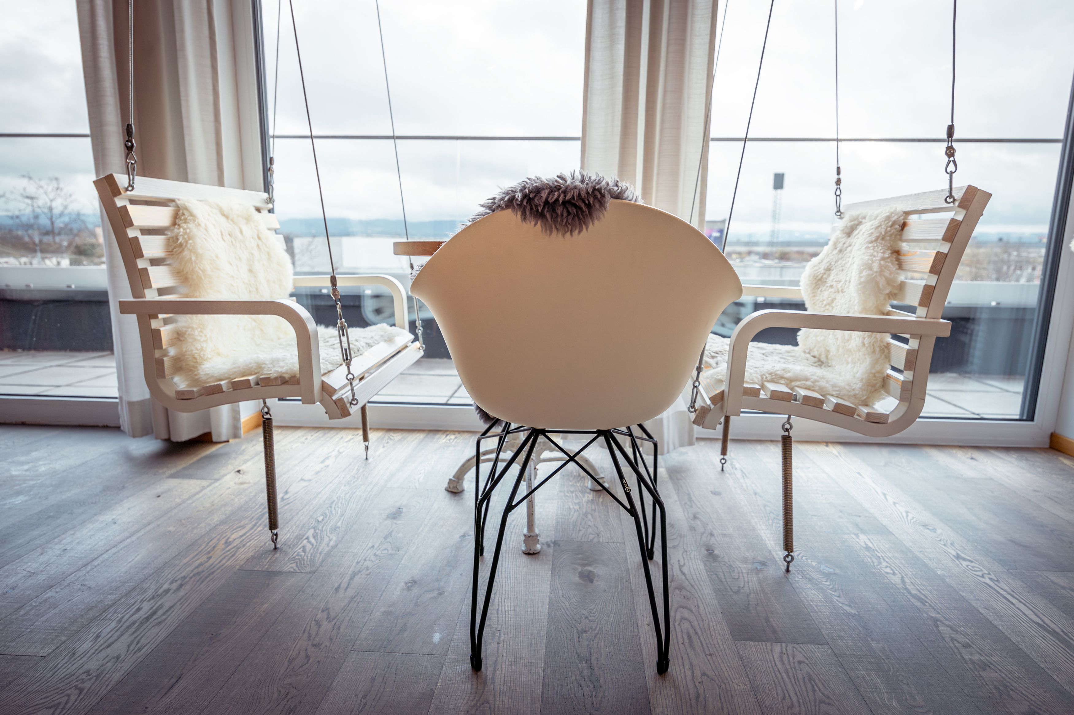 Innenraum mit Schaukelstühlen und einem modernen Stuhl vor großen Fenstern.