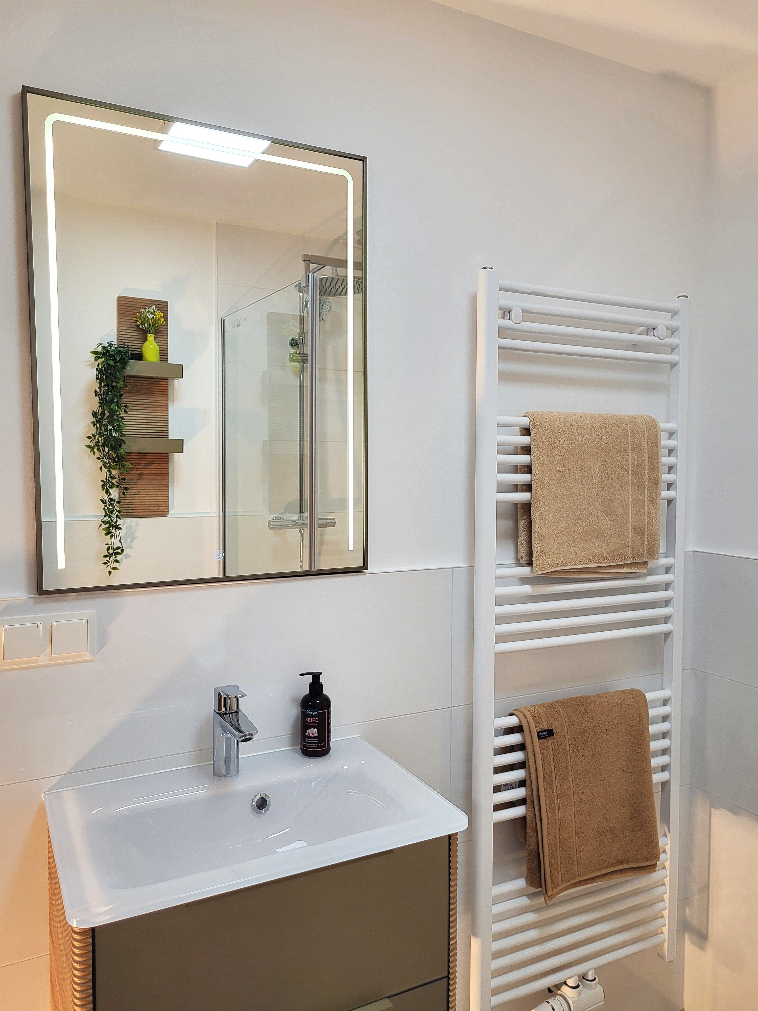 Modernes Badezimmer mit Spiegel, Waschbecken und Handtuchheizkörper.