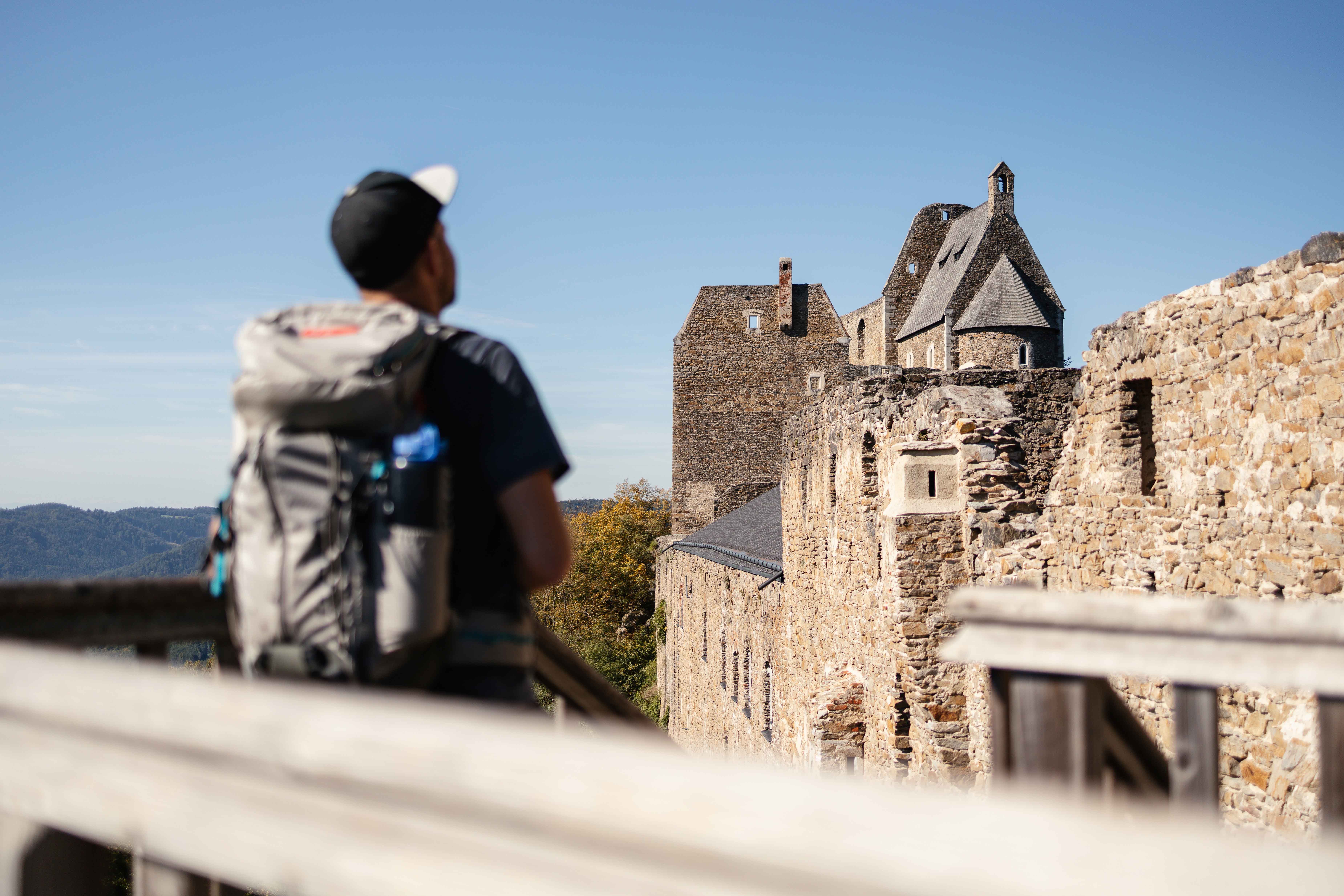 Ein Wanderer mit Rucksack betrachtet die Burgruine Aggstein an einem sonnigen Tag.