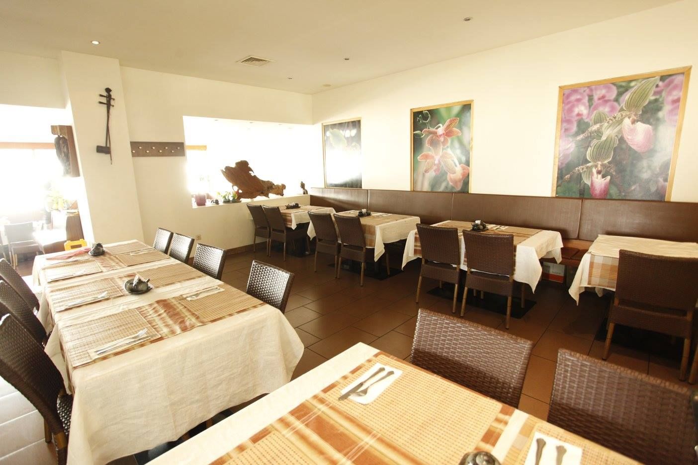 Innenansicht eines Restaurants mit gedeckten Tischen und Blumenbildern an der Wand.