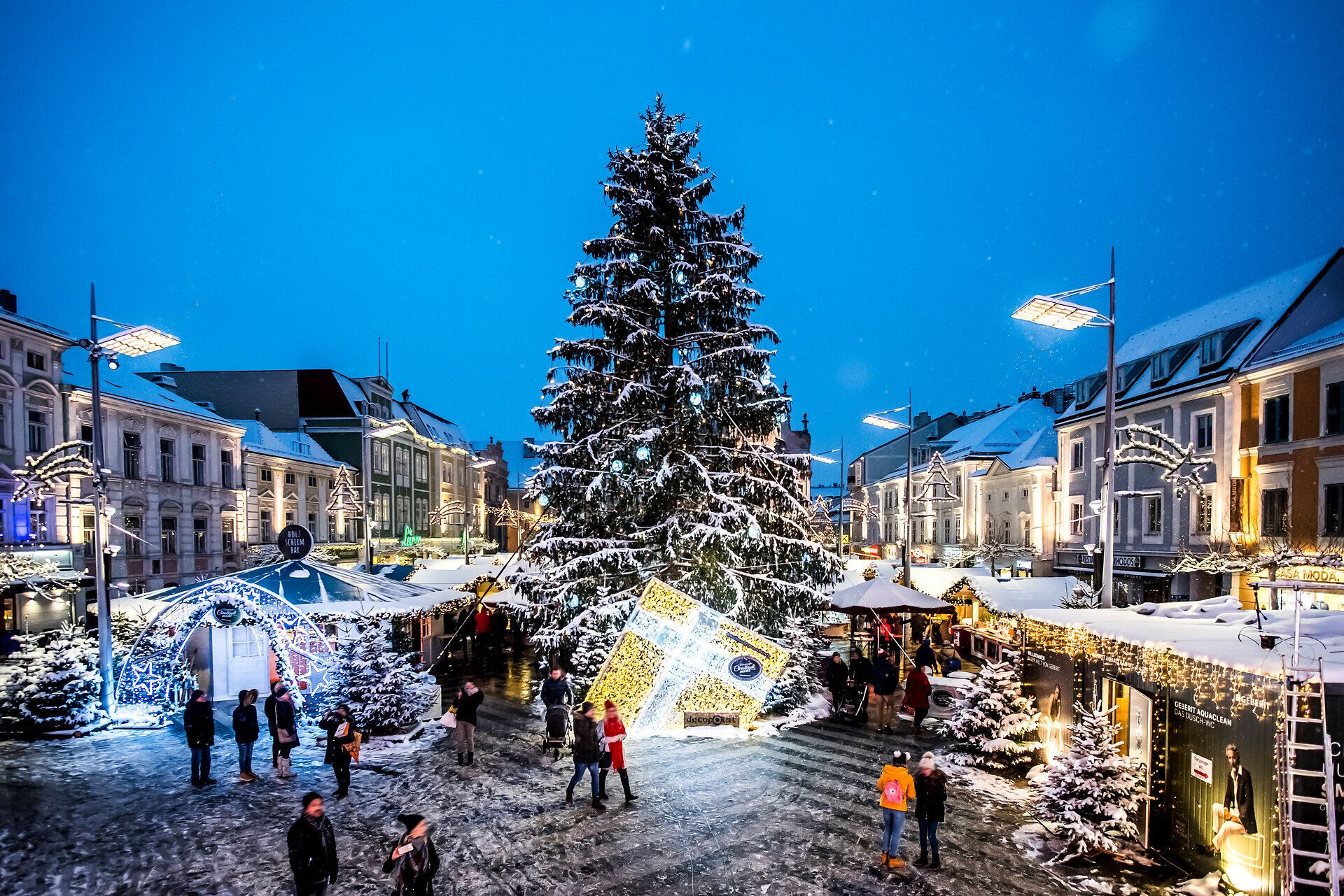 Der festlich geschmückte Adventmarkt erstrahlt in warmem Licht und lädt Besucher ein, die besinnliche Atmosphäre zu genießen. Umgeben von schneebedeckten Bäumen und einem prächtigen Weihnachtsbaum, verbreitet der Markt den Duft von Glühwein und frisch gebackenem Gebäck. Hier wird die Vorfreude auf das Weihnachtsfest spürbar.