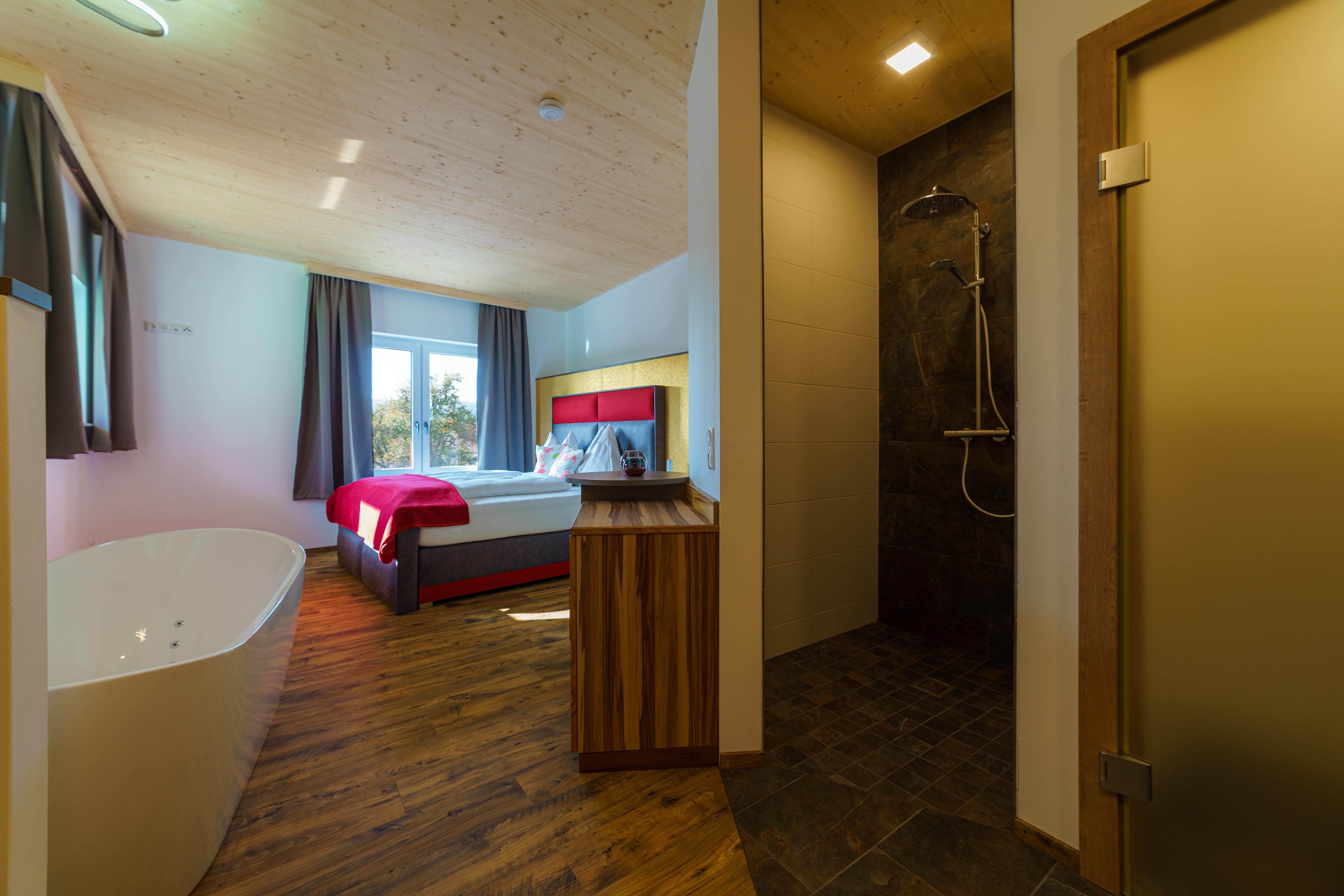 Ein gemütliches Zimmer mit Doppelbett, freistehender Badewanne und moderner Dusche.