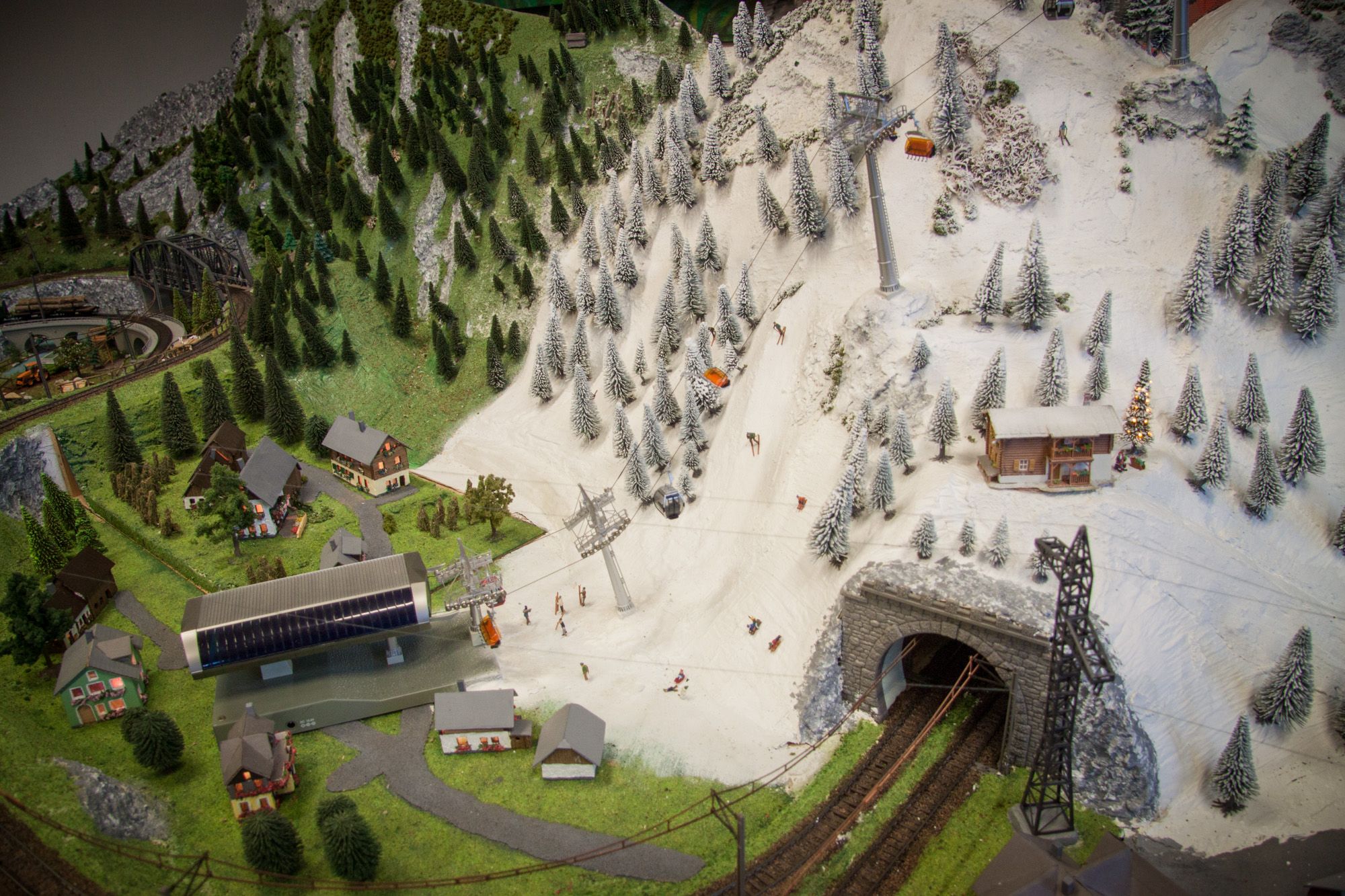 Modelllandschaft mit Bergen, Skifahrern, Seilbahn und Eisenbahntunnel.