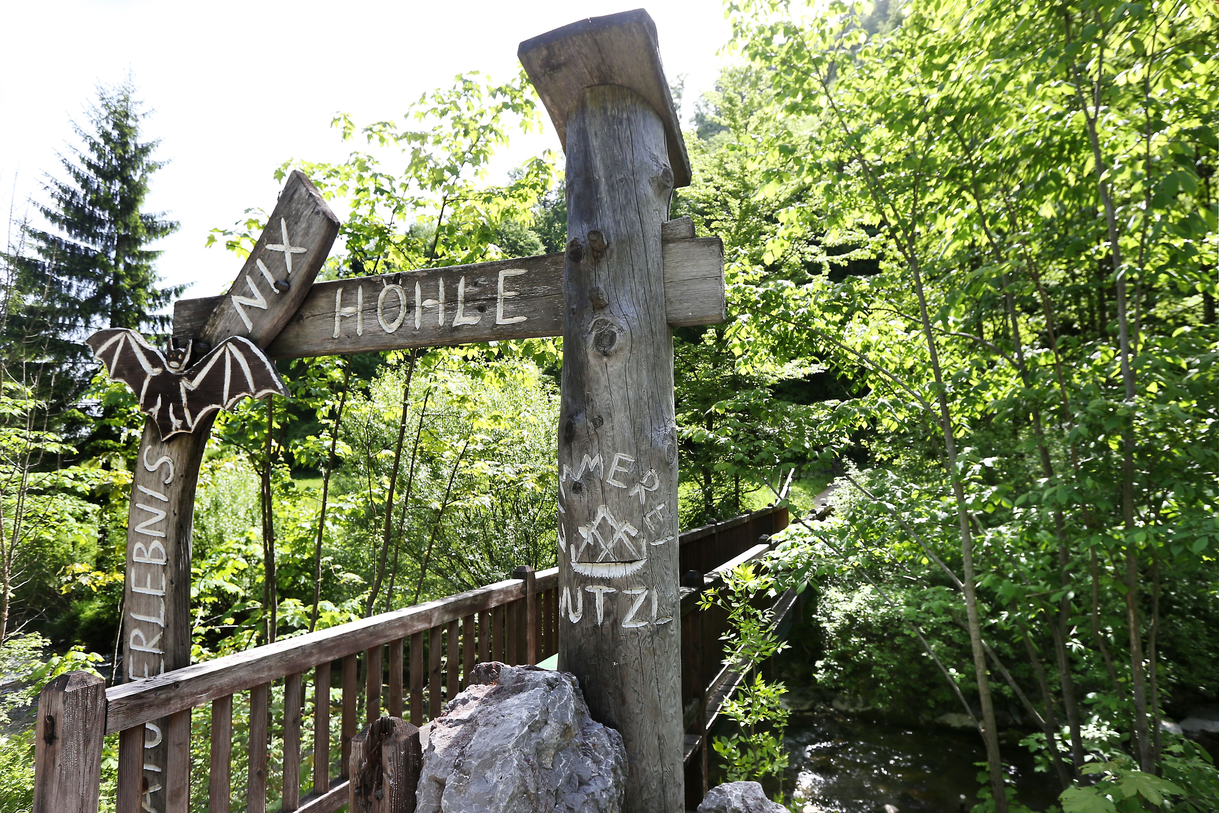 Eingang zur Nixhöhle mit Holzschild und Fledermausdekoration, umgeben von grüner Vegetation.