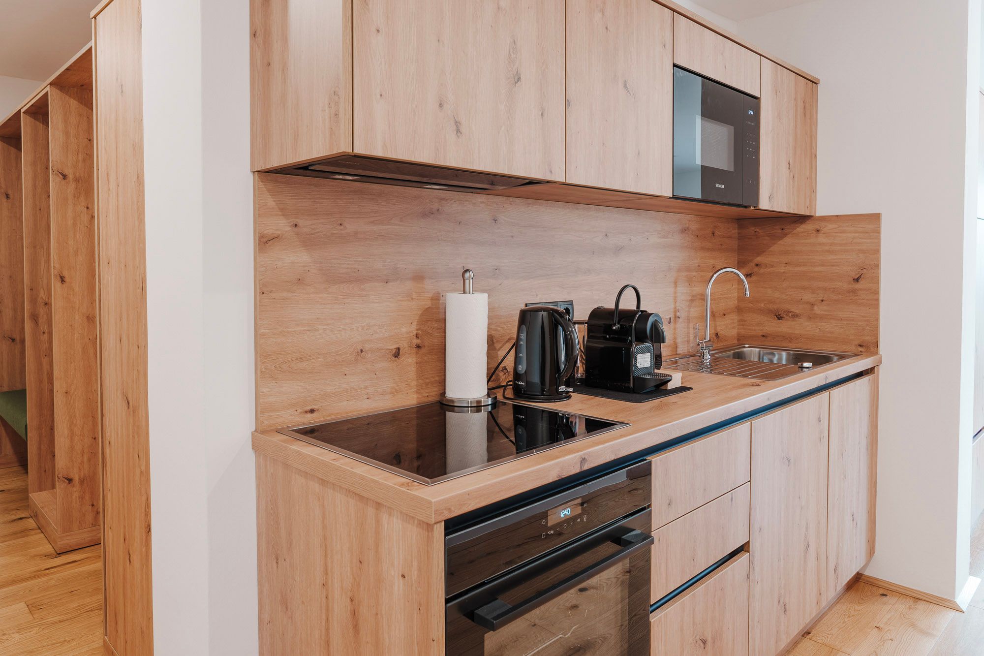 Moderne Küchenzeile mit Holzverkleidung, Kochfeld, Wasserkocher, Kaffeemaschine und Spüle.