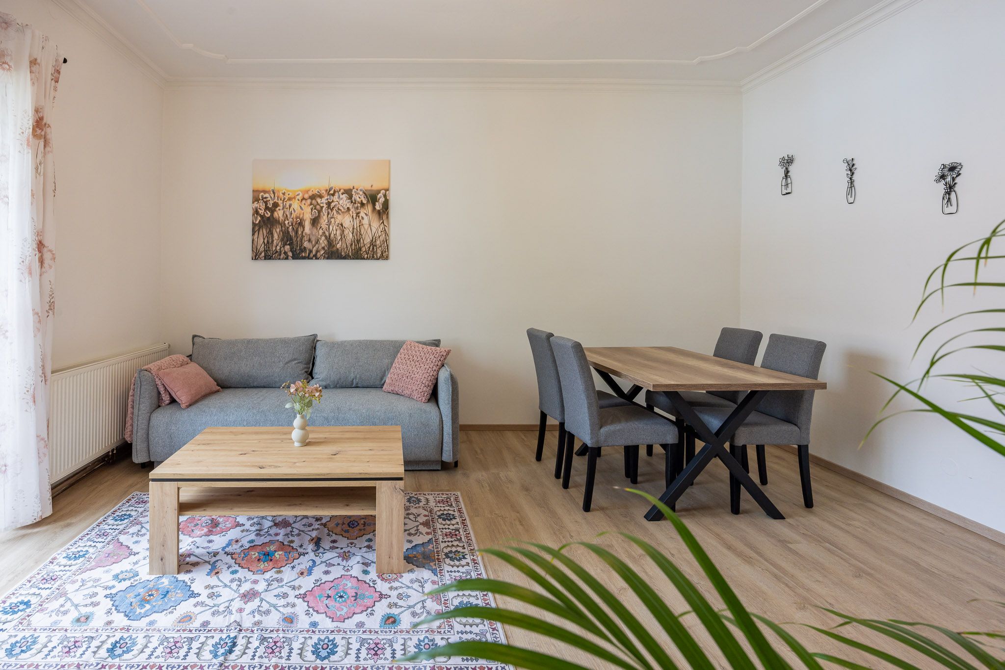 Wohnzimmer mit grauem Sofa, Holztisch, Teppich und Esstisch mit Stühlen.