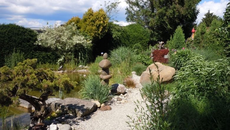 Ein gepflegter Garten mit Kiesweg, Steinskulpturen und üppiger Vegetation.