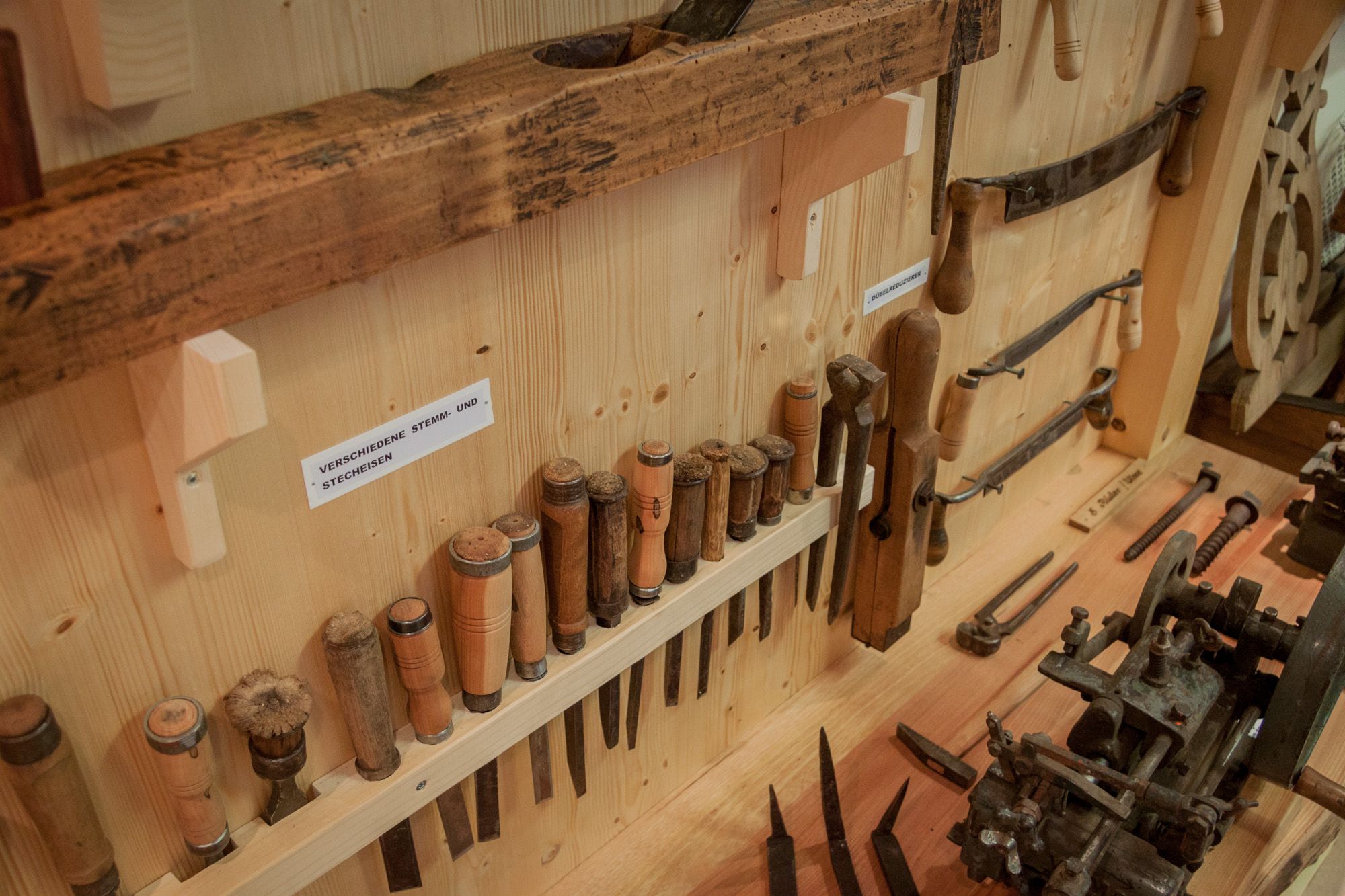 Eine Sammlung von Holzwerkzeugen, darunter Stemm- und Stecheisen, an einer Holzwand ausgestellt.