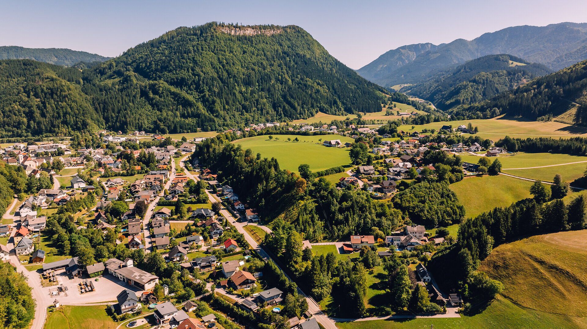 Luftaufnahme von Göstling an der Ybbs mit dem Ortszentrum, grünen Wiesen und bewaldeten Bergen im Hintergrund.