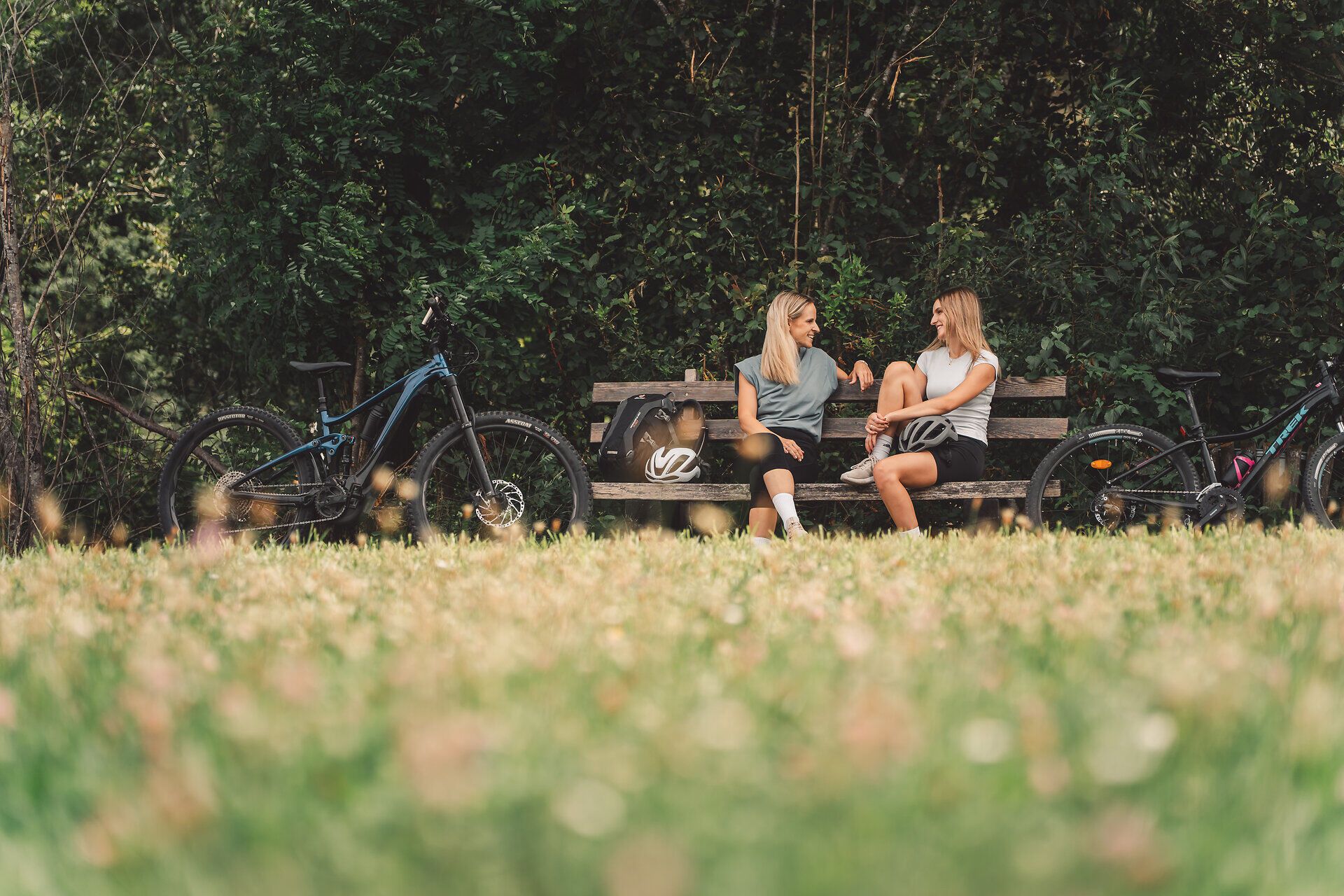 Radfahrerinnen machen bei einer Sitzbank im Grünen Pause.