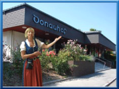Eine Frau in traditioneller Kleidung steht vor einem Gebäude mit der Aufschrift 'Donauhof'.