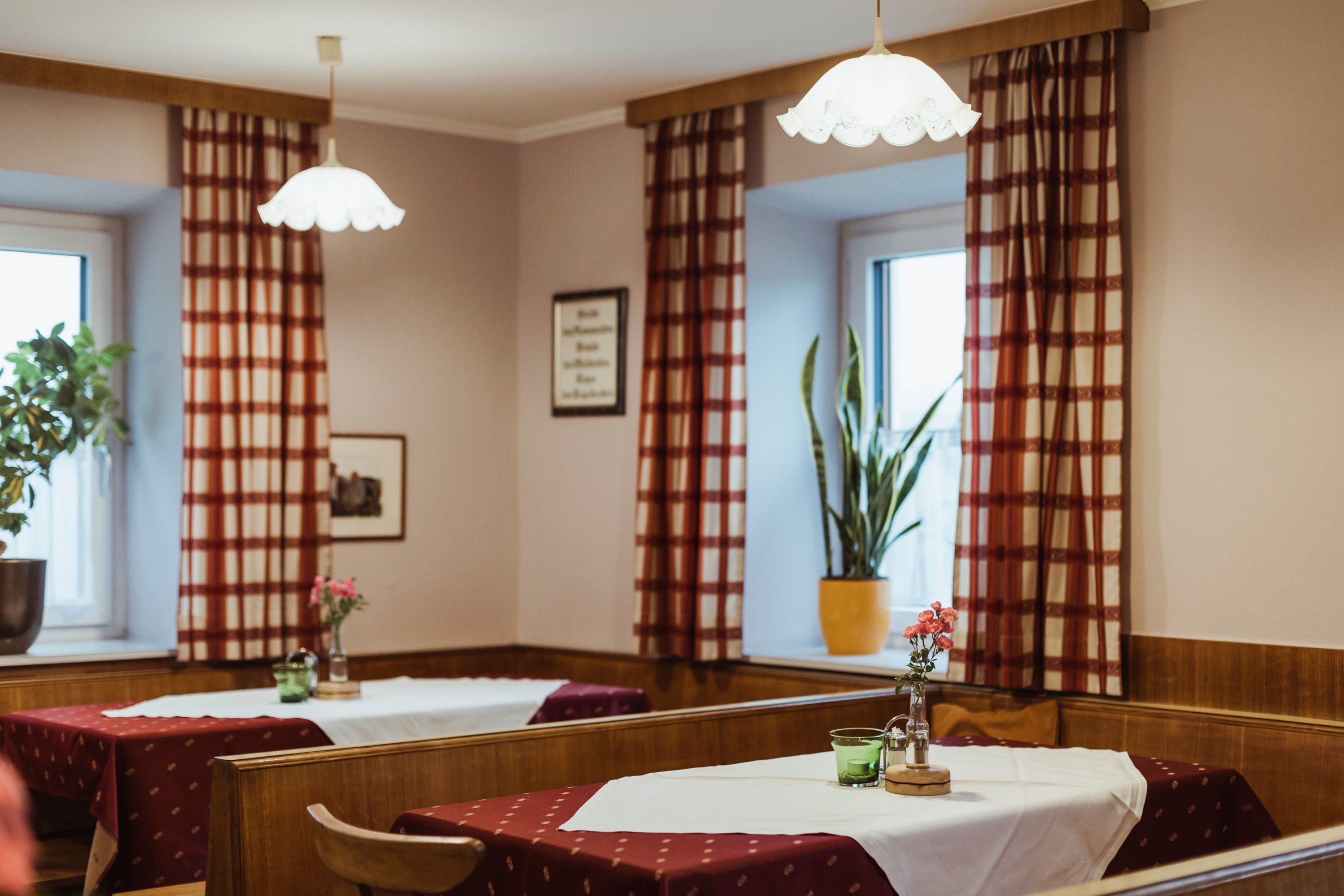 Gemütliche Wirtshausstube mit Holzmöbeln, karierten Vorhängen und dekorierten Tischen.