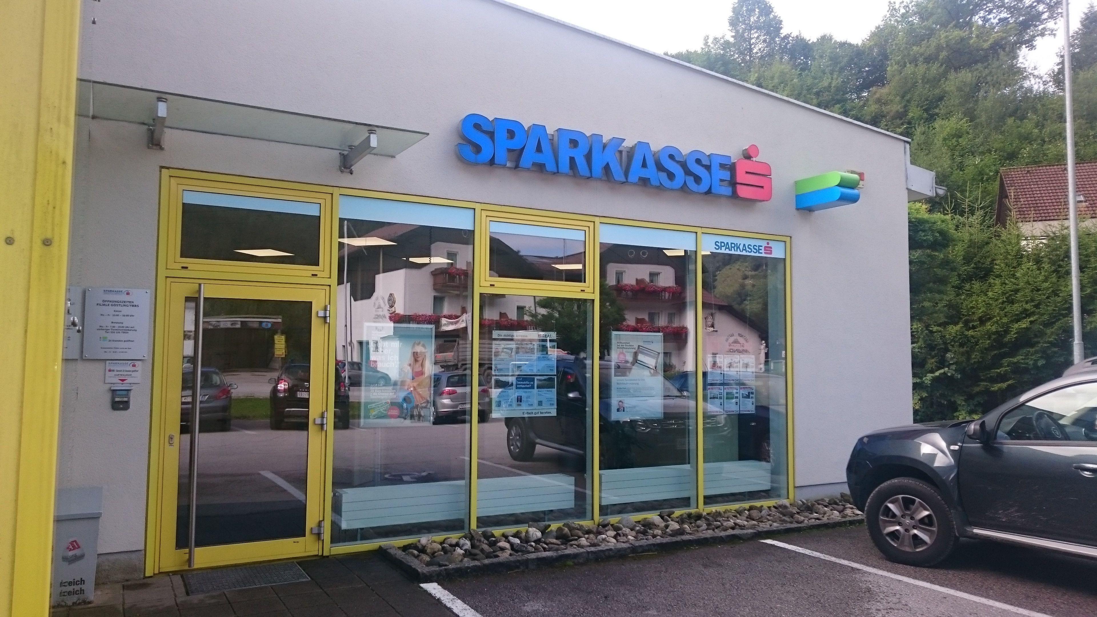 Eingang einer Sparkasse-Filiale mit gelbem Rahmen und Glastüren.
