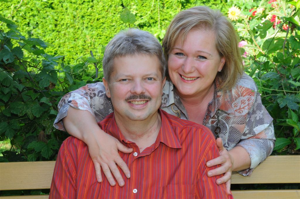 Ein lächelndes Paar sitzt auf einer Bank im Garten.