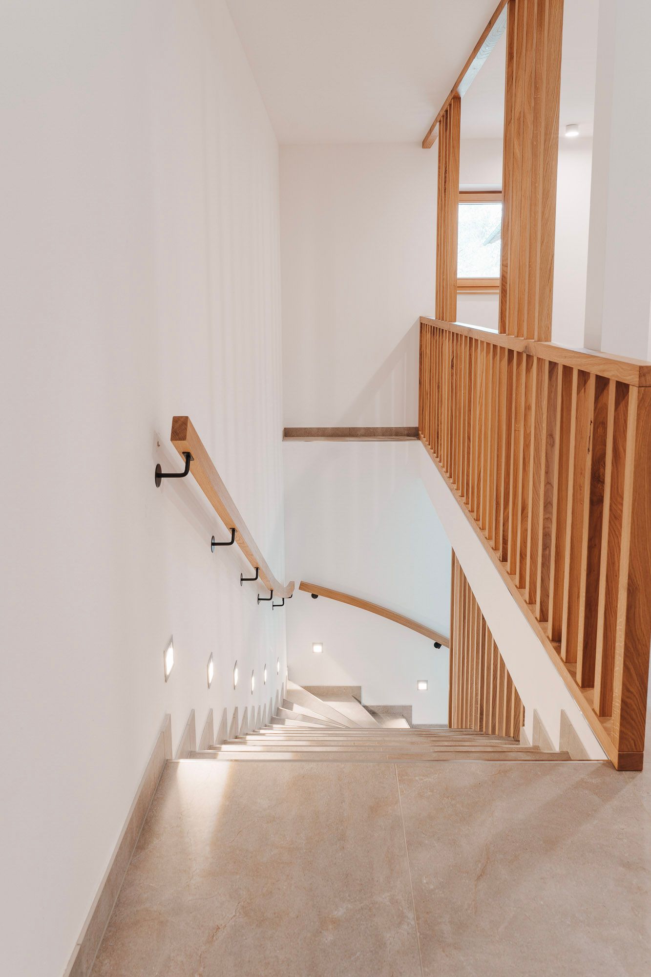 Moderne Treppe mit Holzgeländer und Wandbeleuchtung in einem hellen Innenraum.