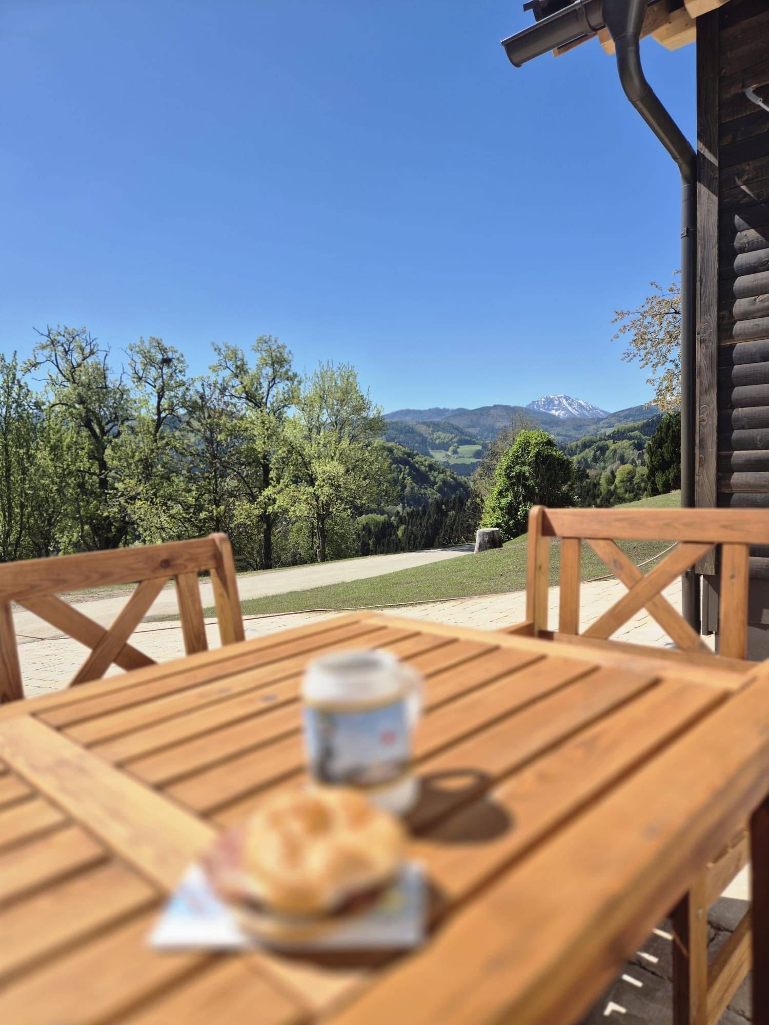 Holztisch mit Getränk und Gebäck im Vordergrund, Berglandschaft im Hintergrund.