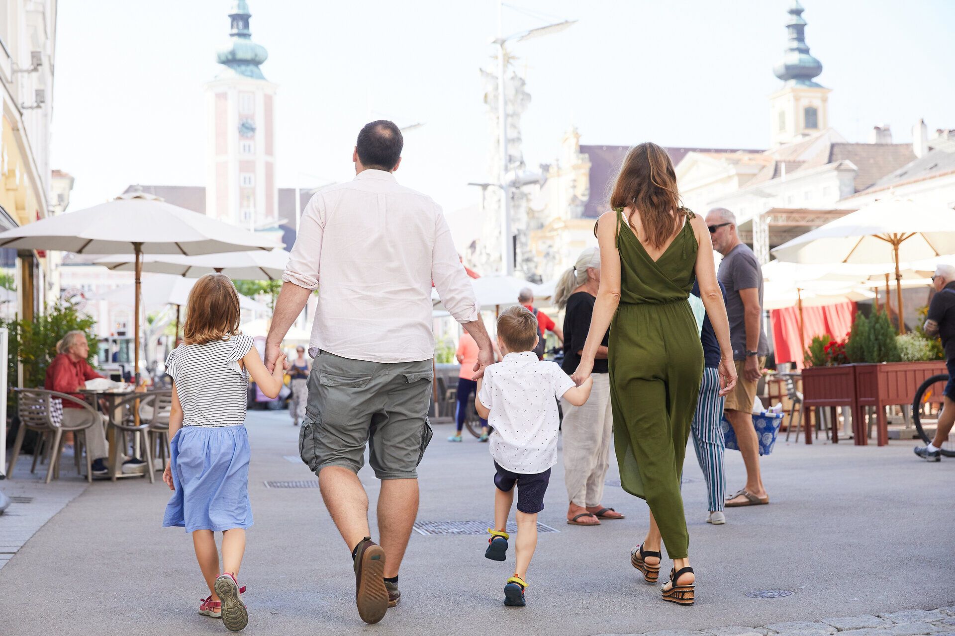 Eine Familie schlendert fröhlich durch die belebten Straßen, während die Sonne warm auf ihre Schultern scheint. Die Kinder lachen und halten die Hände ihrer Eltern, während sie die bunten Stände und Cafés bewundern. Diese lebendige Atmosphäre lädt dazu ein, die Schönheit der Stadt zu entdecken.