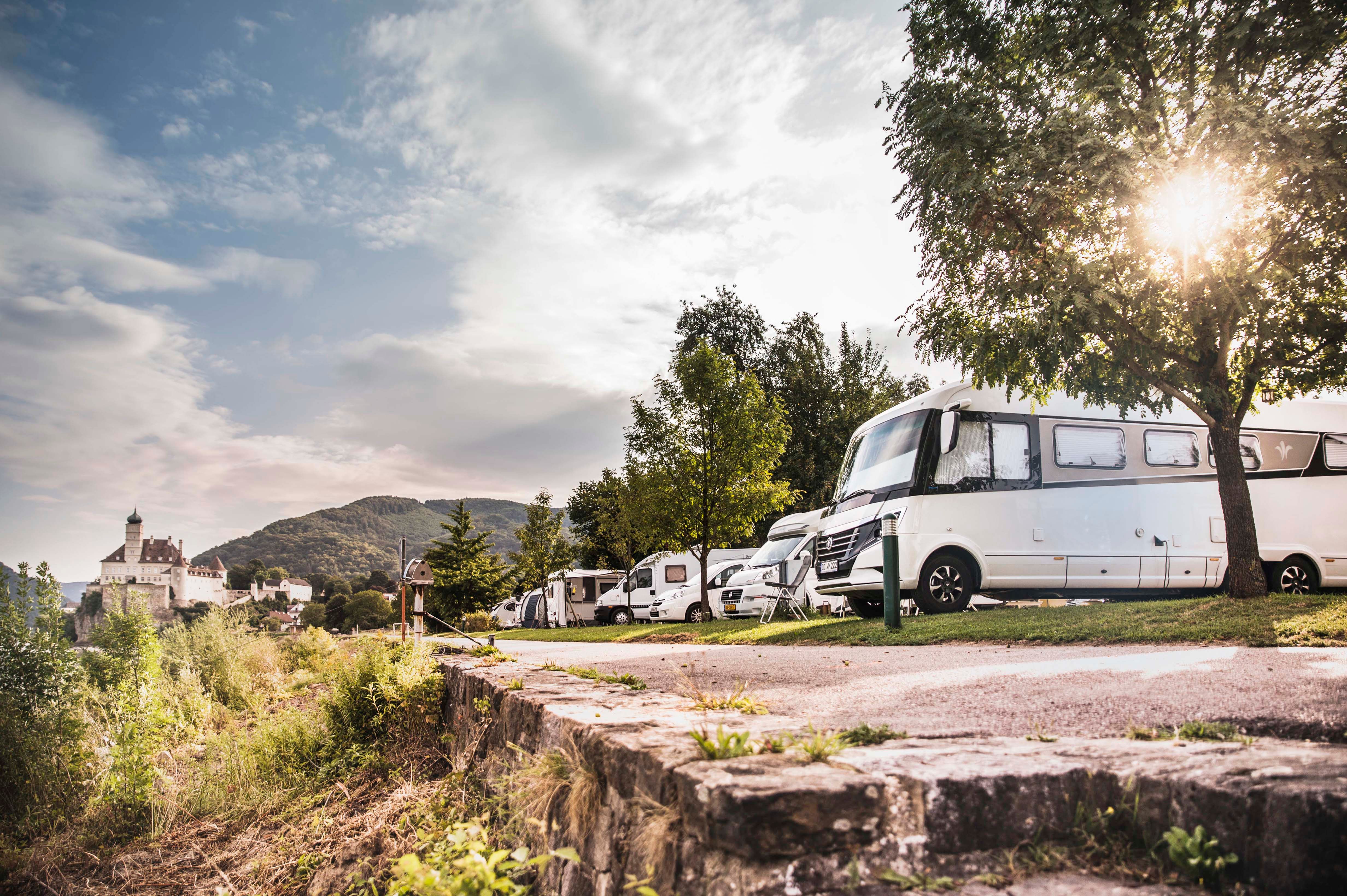 Wohnmobile auf einem Campingplatz mit Schloss im Hintergrund.