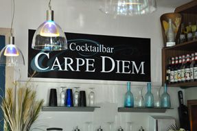 Innenansicht einer Bar mit einem Schild 'Cocktailbar Carpe Diem' an der Wand.