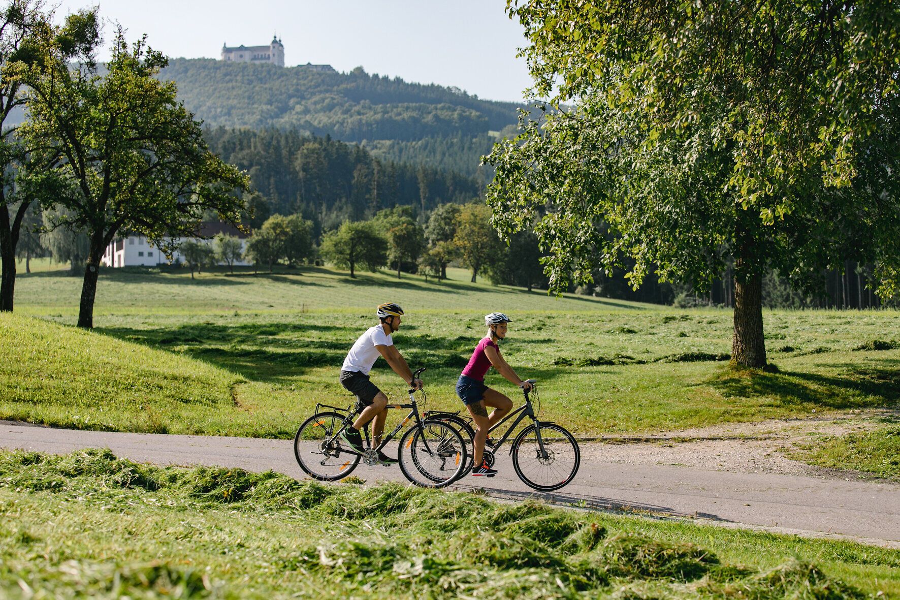 Ein Paar radelt entspannt durch die malerische Landschaft, umgeben von saftigem Grün und sanften Hügeln. Die frische Bergluft und die strahlende Sonne schaffen eine perfekte Atmosphäre für einen aktiven Tag in der Natur. Die idyllische Umgebung lädt dazu ein, die Schönheit der Region zu entdecken und die Seele baumeln zu lassen.