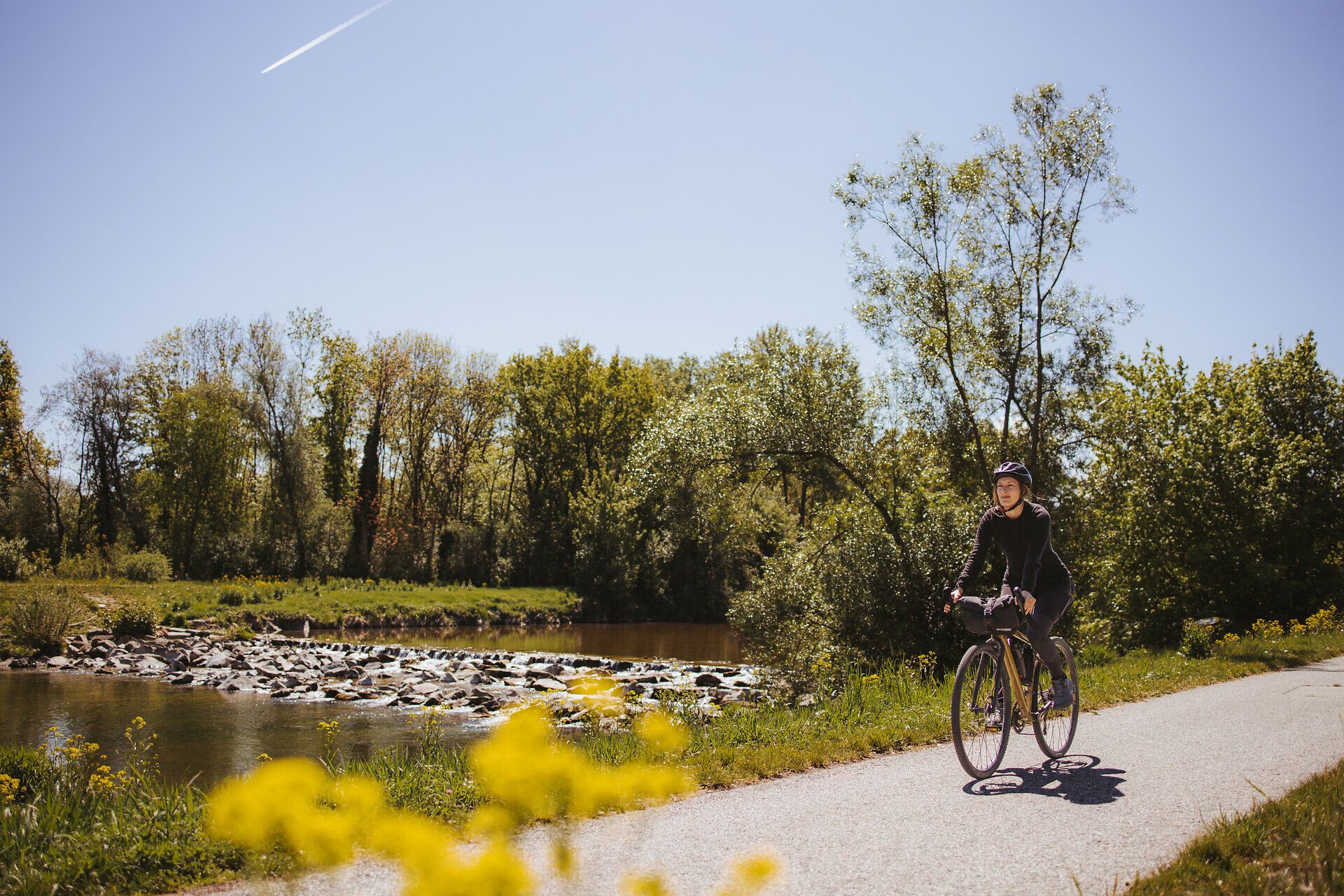 Ein sonniger Tag am Traisental-Radweg lädt Radfahrer ein, die malerische Landschaft zu erkunden. Umgeben von üppigem Grün und blühenden Wildblumen, gleitet man sanft entlang des ruhigen Flusses, während die sanften Hügel im Hintergrund eine idyllische Kulisse bieten.