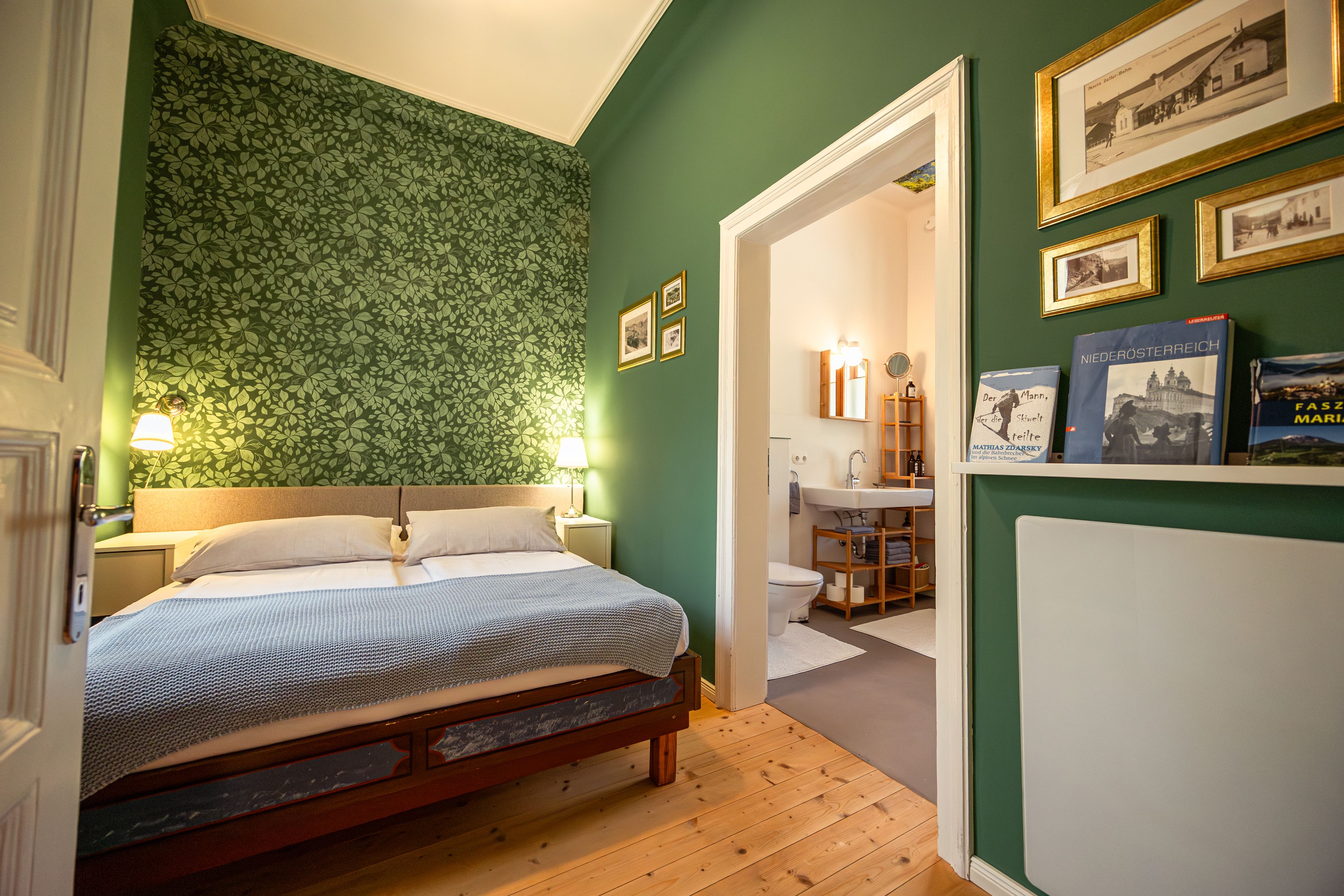 Gemütliches Schlafzimmer mit grün gemusterter Tapete, Doppelbett und angrenzendem Badezimmer.