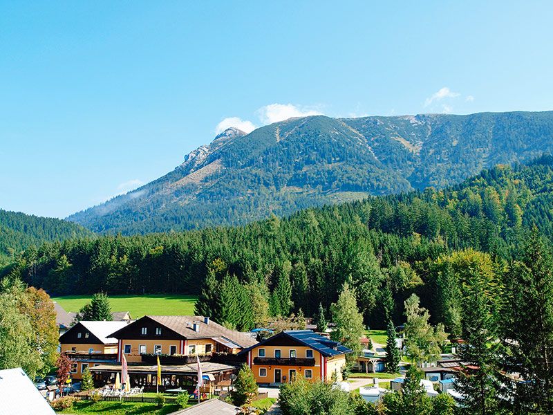 Blick auf ein Campinggelände mit Gebäuden vor einem bewaldeten Bergmassiv.