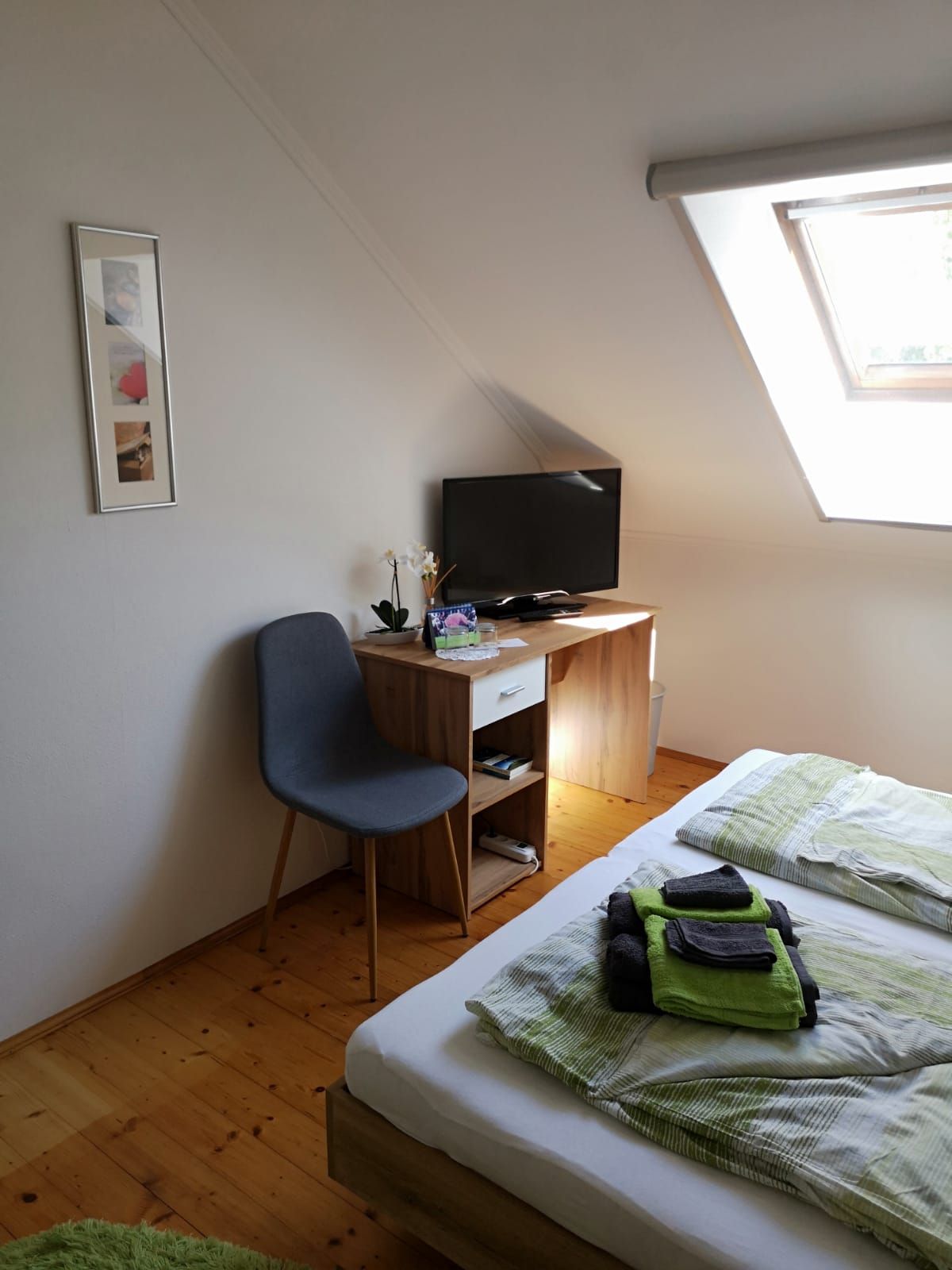 Ein gemütliches Zimmer mit einem Bett, einem kleinen Schreibtisch mit Fernseher, einem Stuhl und einem Dachfenster.