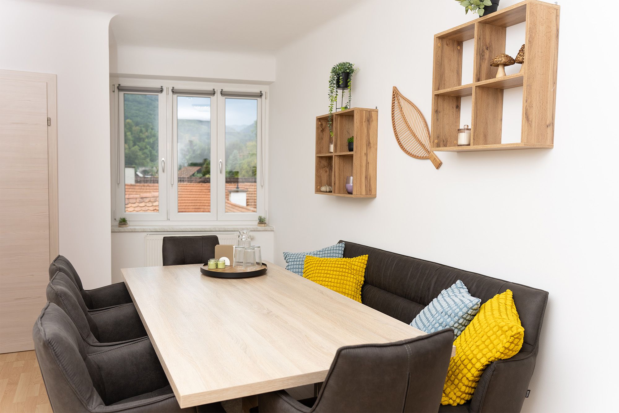 Essbereich in der Ferienwohnung Turmblick mit Holztisch, dunkler Eckbank, Stühlen und Blick aus dem Fenster auf Dächer und Berge.