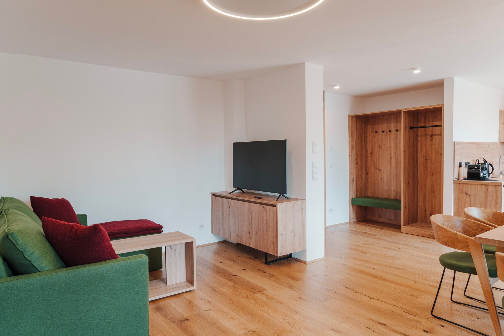 Modern eingerichtetes Wohnzimmer mit grüner Couch, Holzmöbeln und einem Flachbildfernseher.
