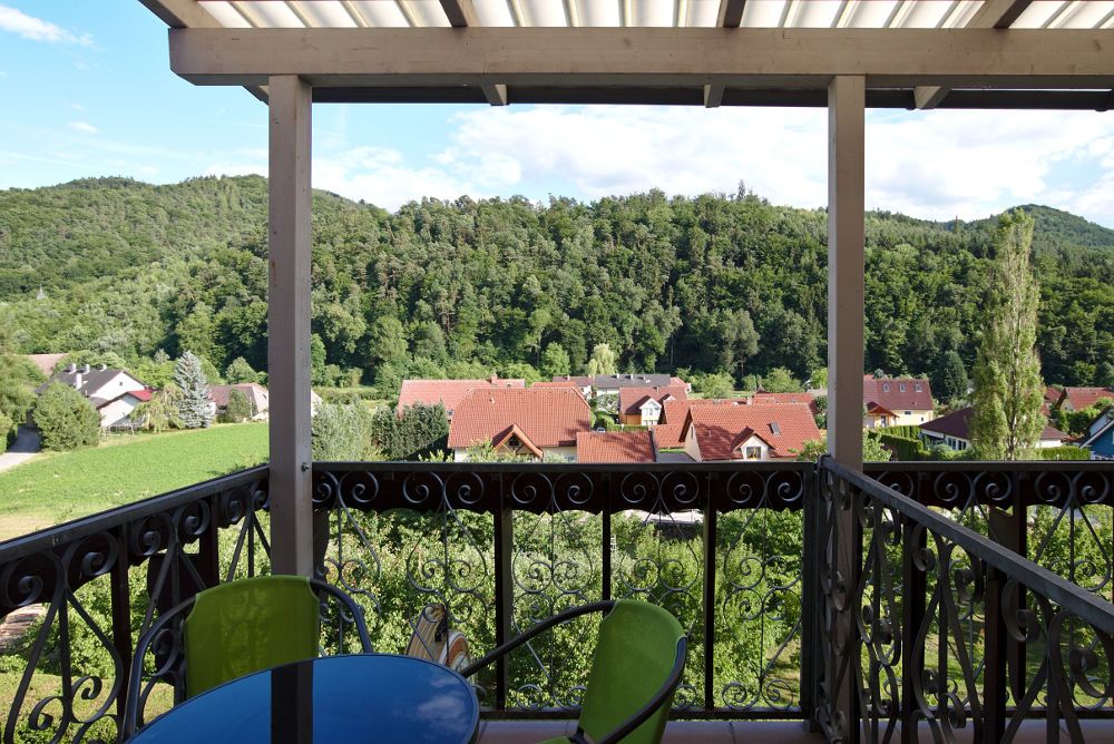 Blick von einem Balkon auf eine grüne Landschaft mit Hügeln und roten Dächern.